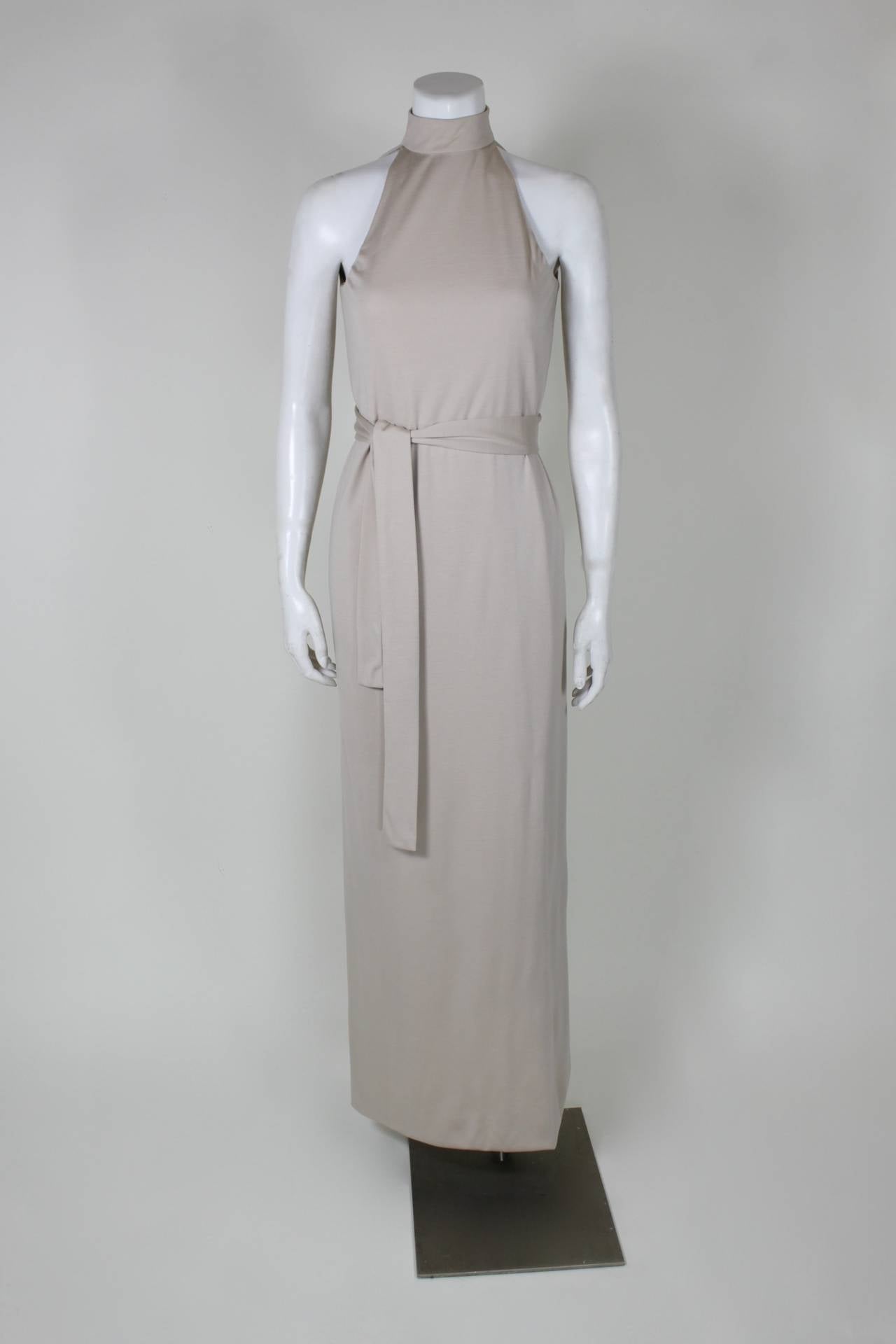 Renowned for the elegance and simplicity of his designs, this gown from legendary American designer Norman Norell is made of luxurious cream wool. Done in a simple belted column silhouette with a halter turtle-neck. The gown features a sexy cutout