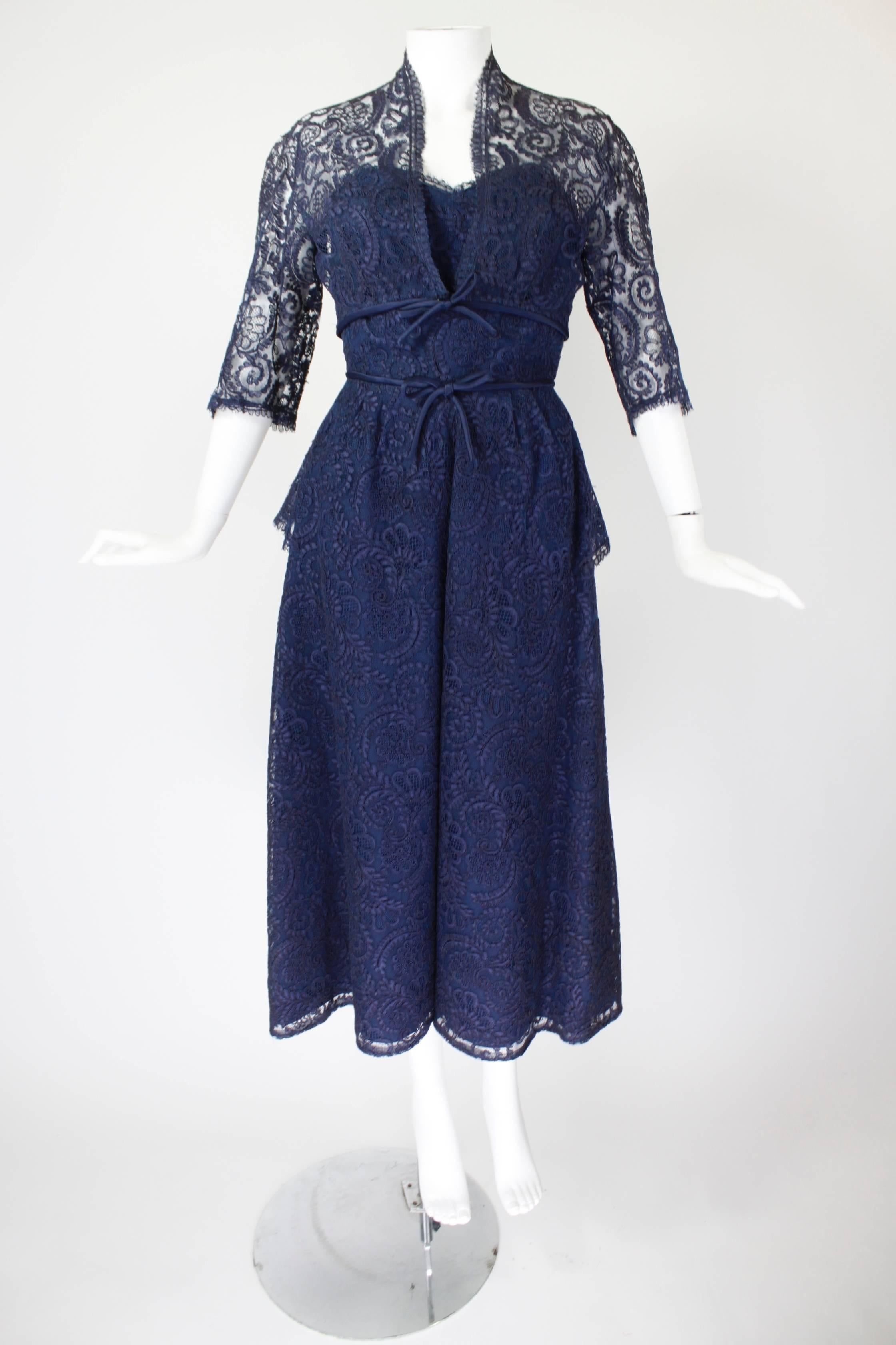 Done in gorgeous navy blue guipure lace, this strapless Jean Desses cocktail dress features a nipped waist, full skirt, and sweetheart neckline. The waist has a peplum on either side of the hip. A matching 3/4 length sleeve bolero compliments the
