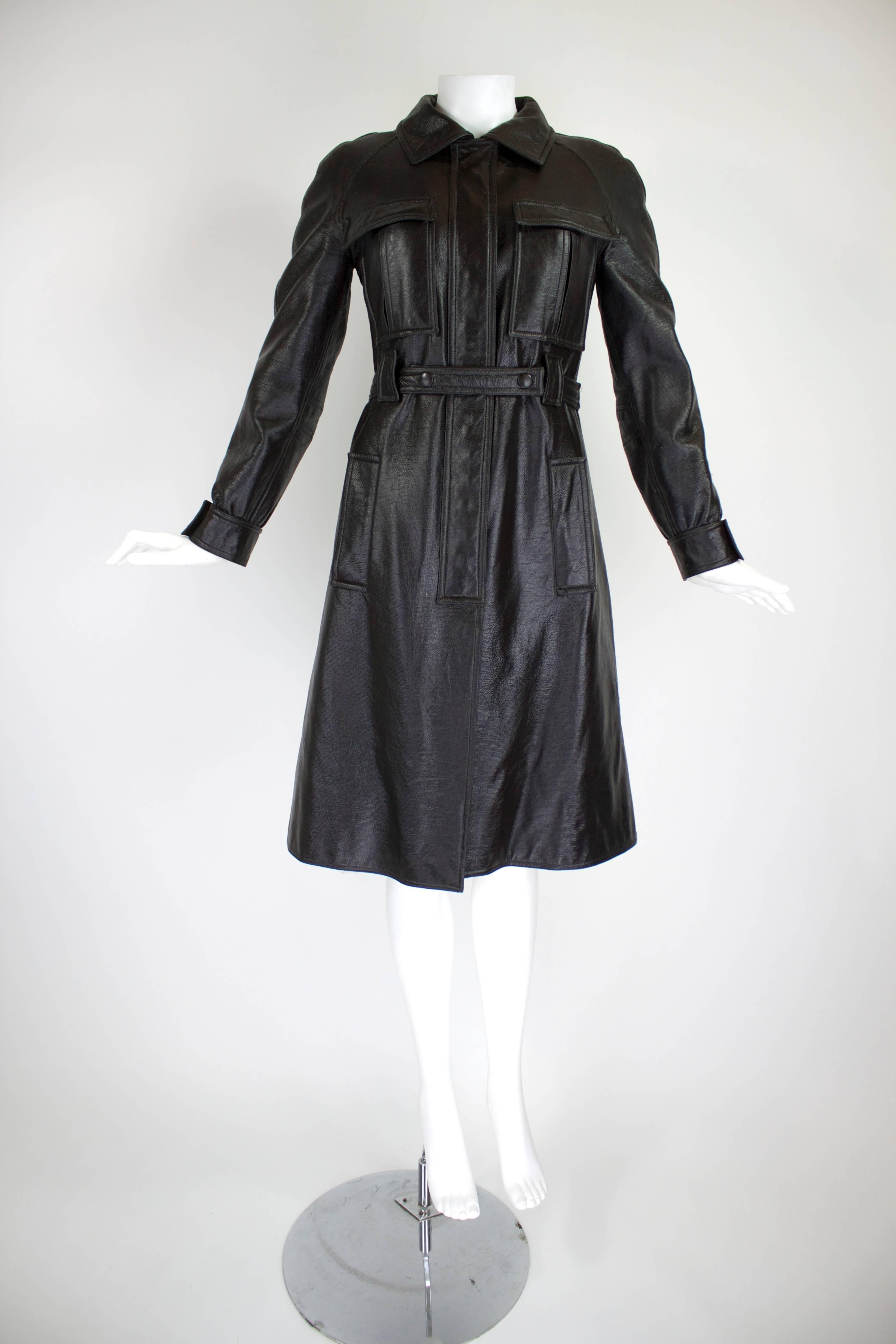 An iconic 1960s Courrèges vinyl trench coat with matching belt. The button-front silhouette features four functional snap pockets. Center seam in back at hem features three snap closures for fit flexibility. Fully lined in fleece.

Bust: 34