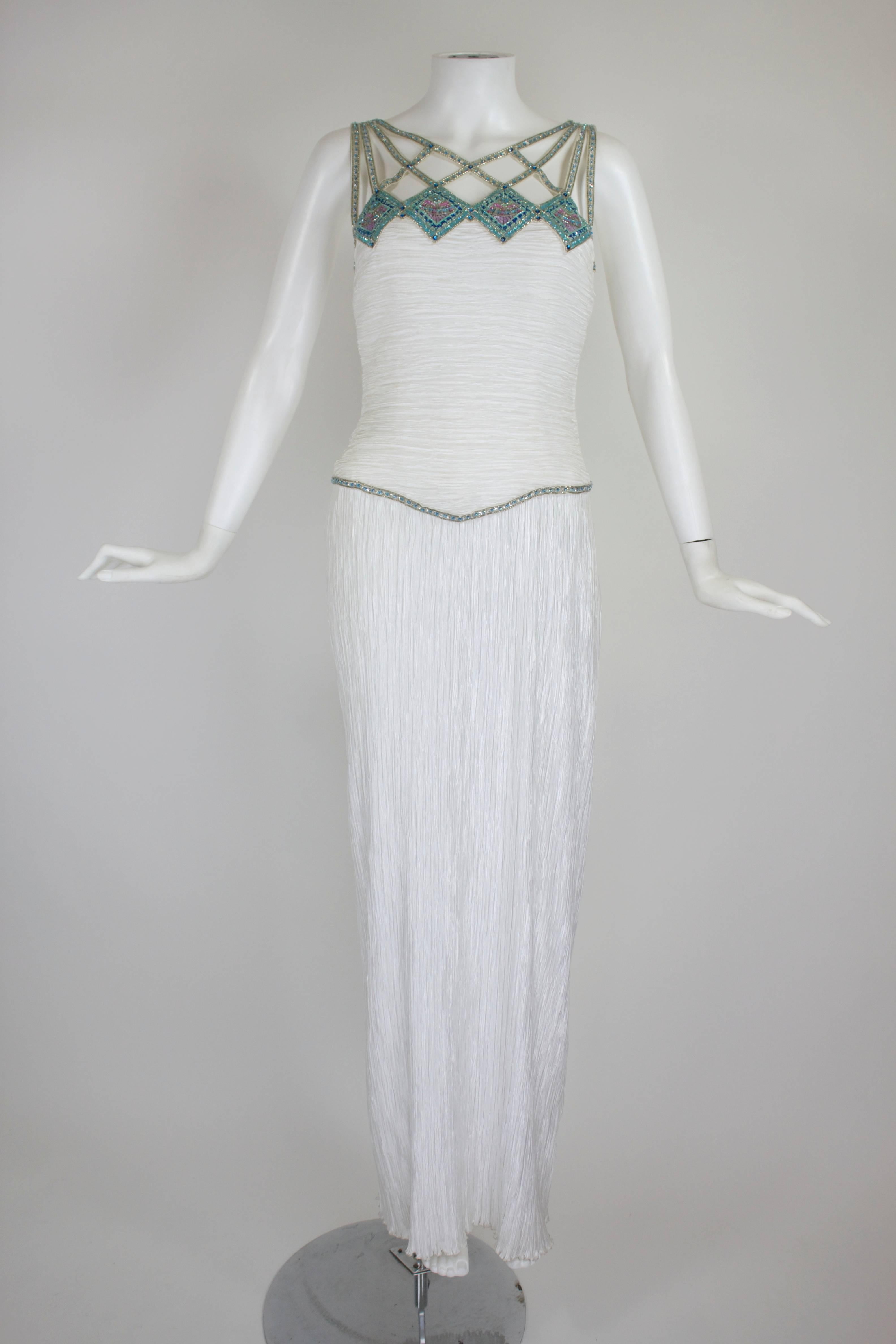 Done in Mary McFadden's iconic micropleats, this gorgeous white column gown features Egyptian revival-inspired beading in a cage pattern across the bodice and shoulders. The fitted bodice allows for a body-skimming, sexy silhouette.
