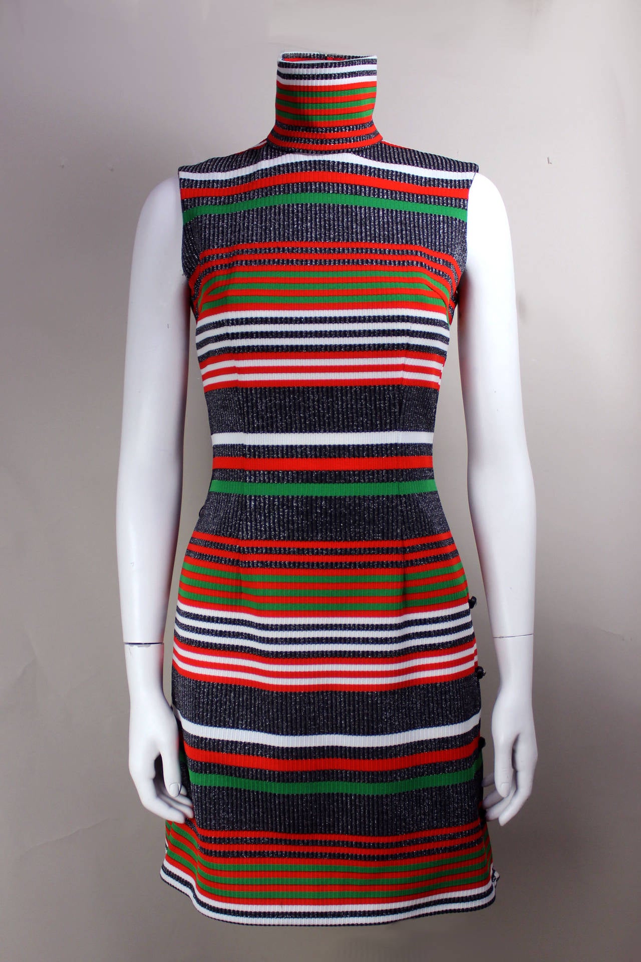 This late 1960s/early 1970s striped knit dress is very appealing with lovely design details. The background is a silver lurex knit with red, white, black, and green stripes. The skirt is a slight A-line with a row of rhinestone buttons along the