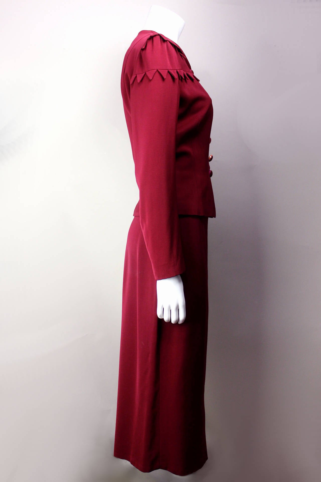 SALE! Originally $495
This 1940s suit is embellished with chevron-shaped flaps in two rows across the shoulders, which form a very unique design element. The buttons are covered to match the deep burgundy fabric of the suit and are ringed by a gold