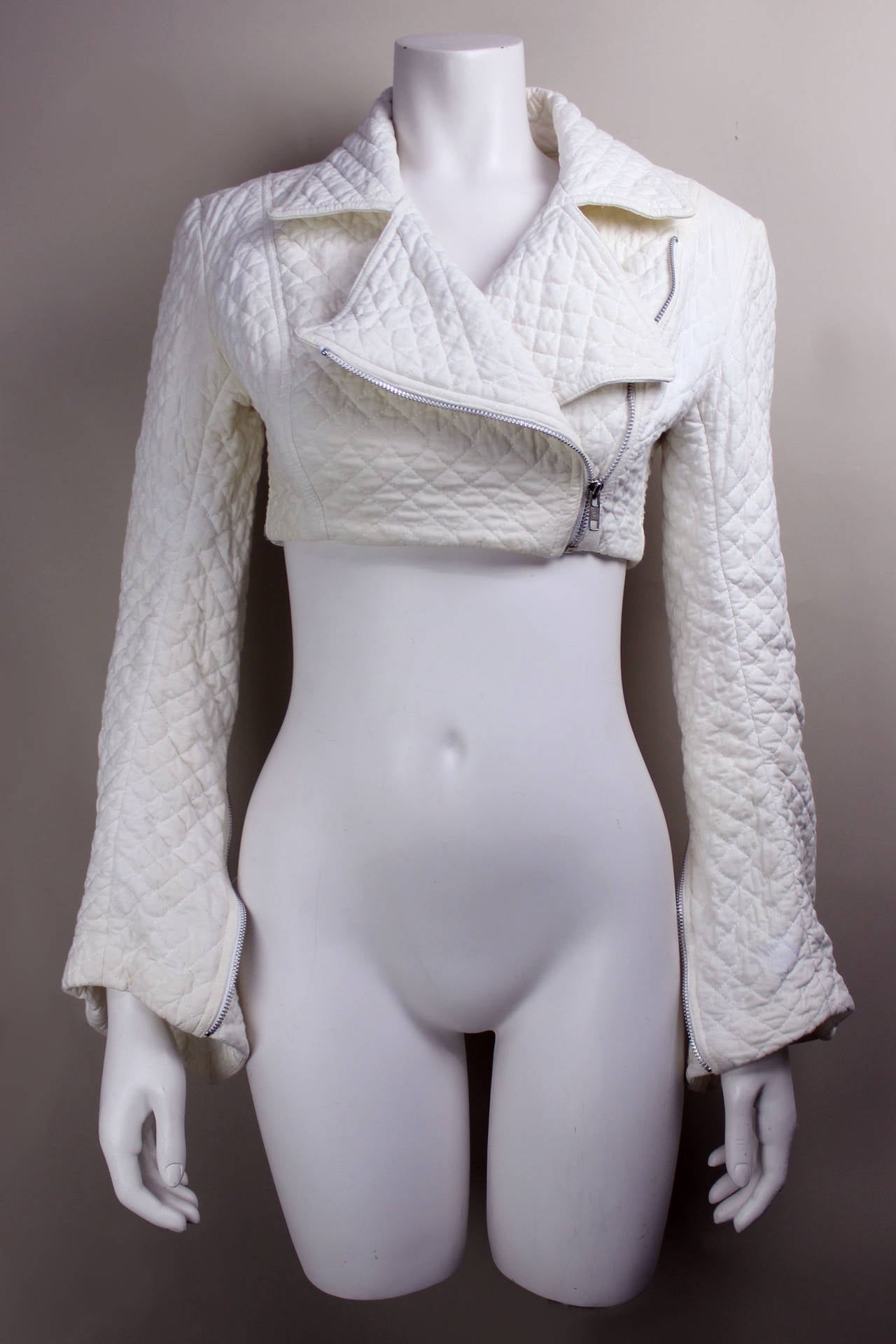 This Norma Kamali jacket is an exceptional piece. It is very cropped with long narrow sleeves that can be unzipped into an exaggerated bell shape. It is of cream-colored quilted fabric and has a side zip in the style of a motorcycle jacket.
