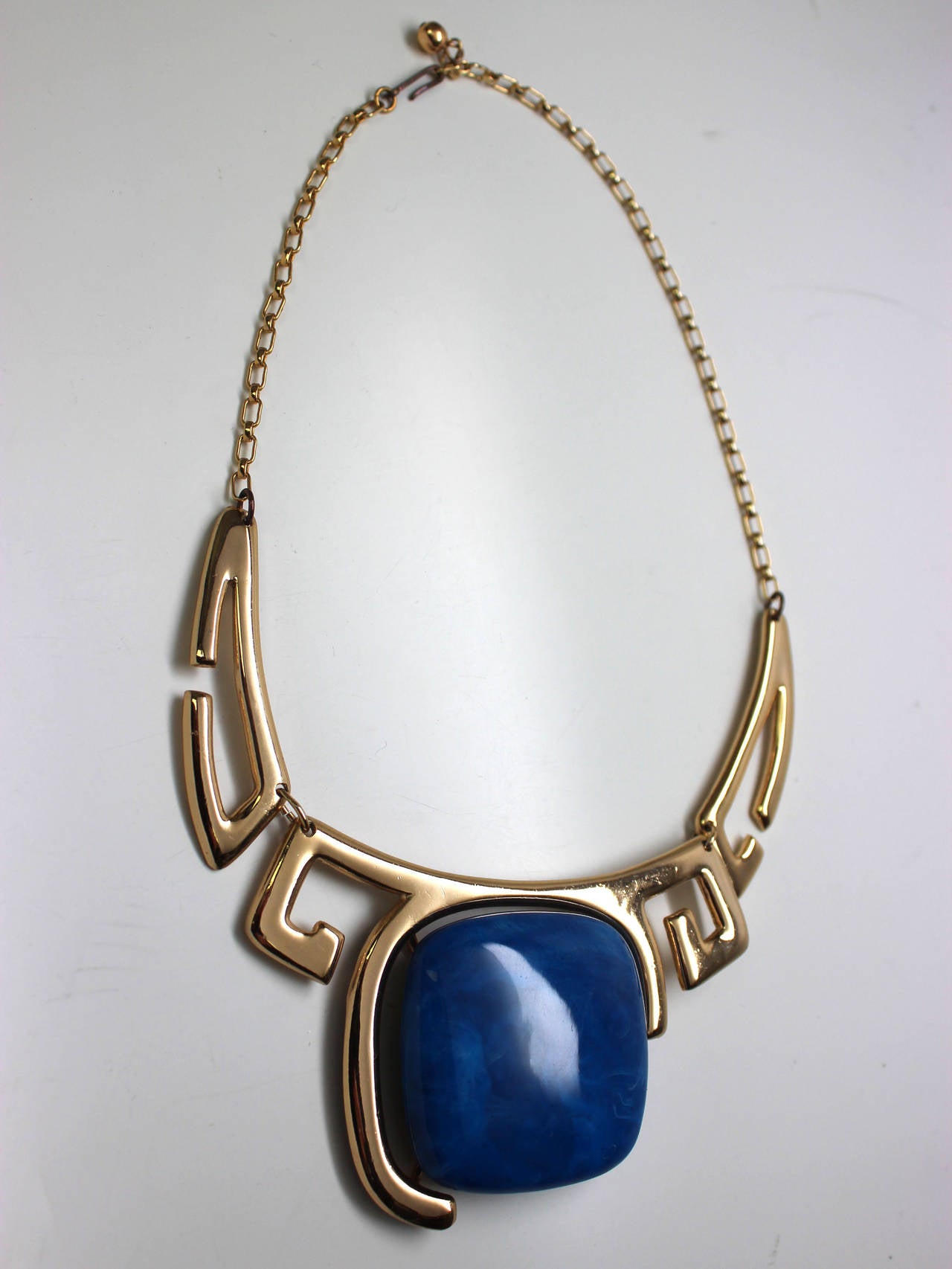 This gorgeous LANVIN necklace has a large blue lucite stone with a frame of asymmetrical Egyptian inspired gold plated pieces. The perfect size and design to rest at the collarbone, this necklace has a hook closure to allow for the length to be