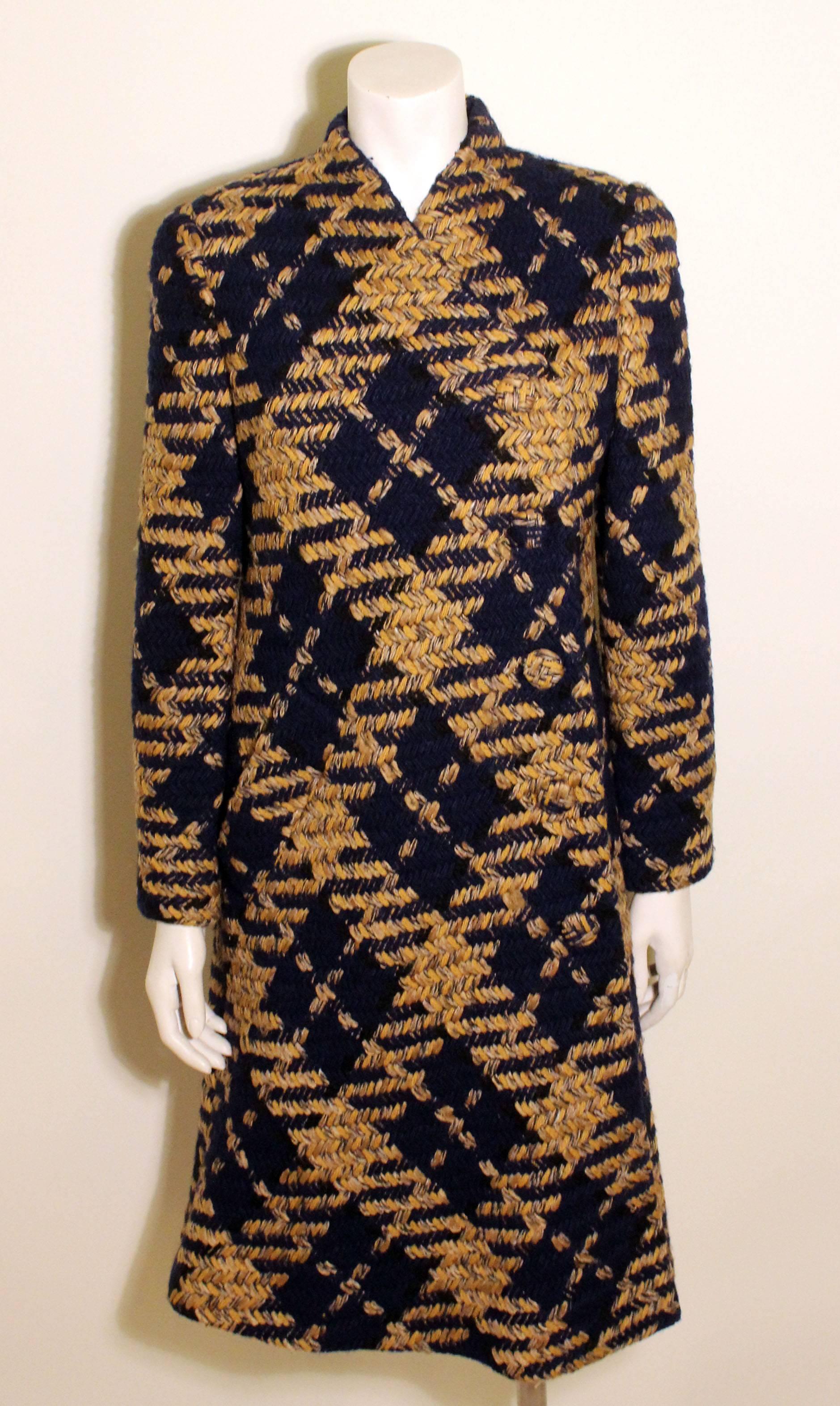 This Trigere coat is a beautiful navy, gold, and mustard tweed. It has interesting detail in that it closes on the diagonal with covered buttons and has a single front pocket.