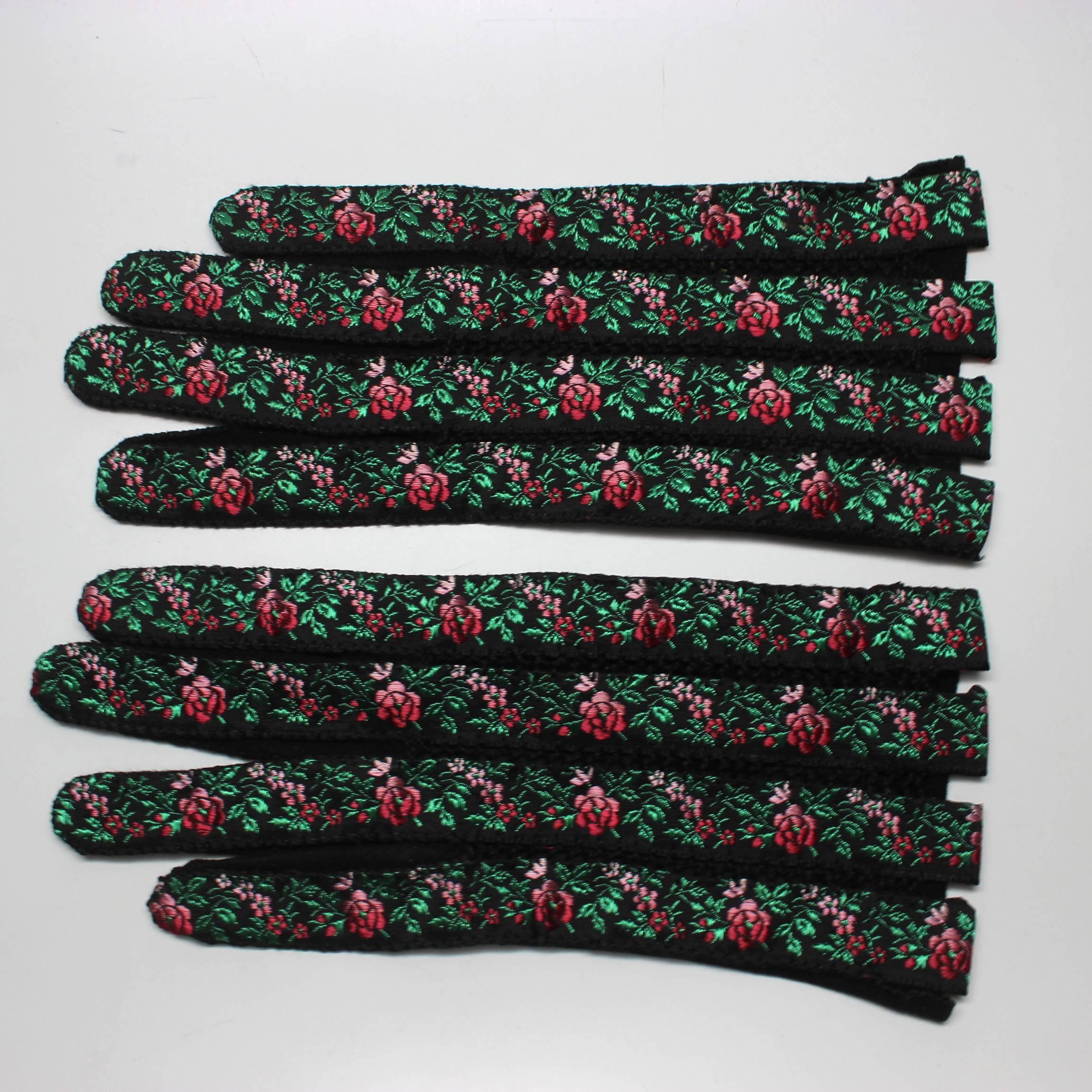 These vintage embroidered gloves are a beautiful floral on strips of ribbon with delicate crochet between the fingers The design is a vibrant green with ombre rose to red flowers on the black glove. The underside is a supple suede. 
Approximate size