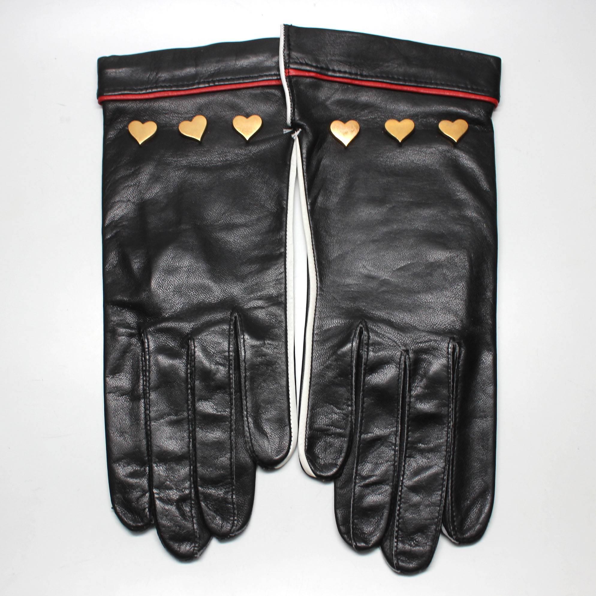 These 1980's Escada gloves are a rare find! Perfect for Valentines Day, and to add to any outfit, these black leather gloves have three gold heart studs on the front, red piping at the wrists, and white piping along the side. They have never been