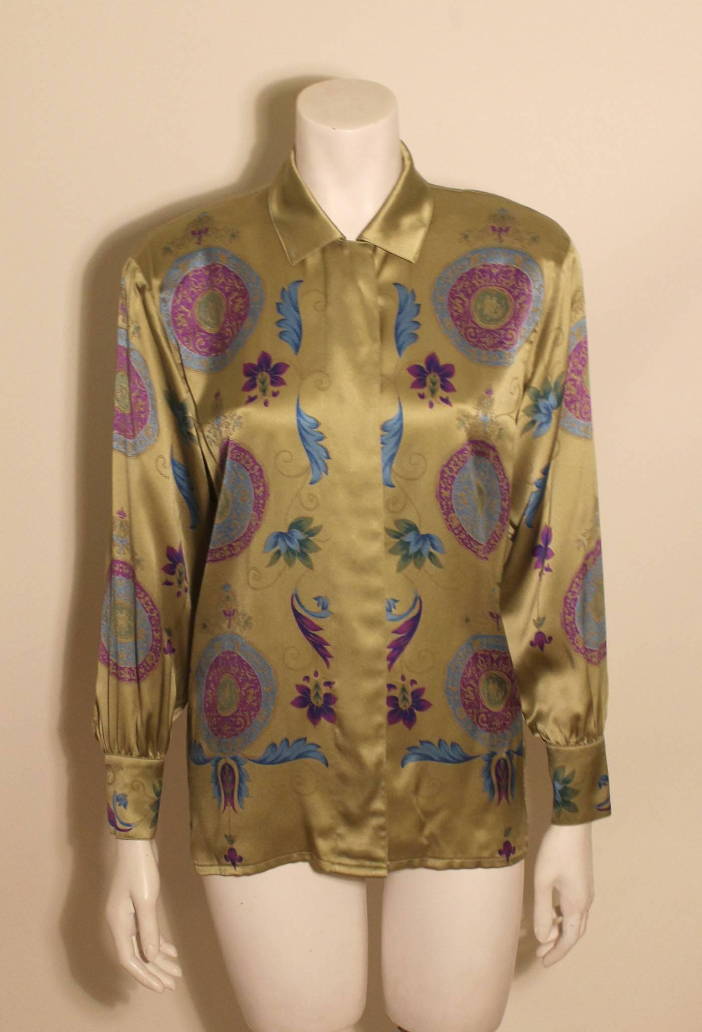 100% silk vintage blouse from Escada featuring a jewel tone pattern of florals and medals on a rich gold/olive background. It has a sleek hidden placket front and two buttons at the sleeves. 