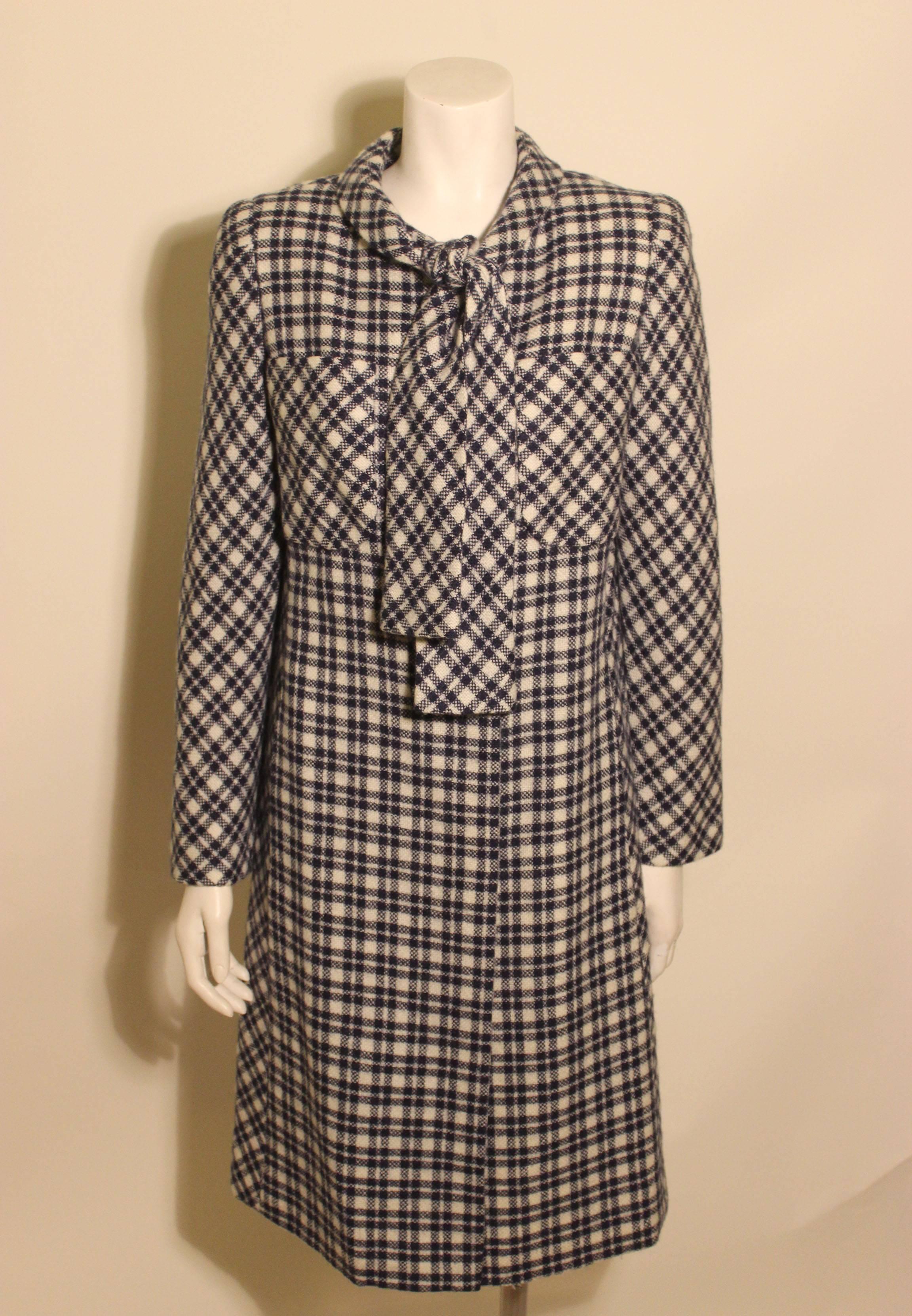1960s style Pauline Trigere coat in a bold navy check with an attached scarf/tie at the stand up necklace. There are two patch pockets above the bustline. 