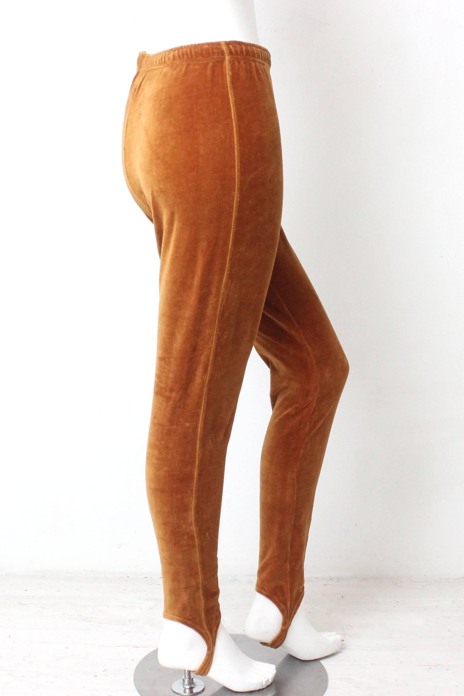 This pair of Moschino Jeans stirrup pants are a twist on a jogging pant. The fabric is a lush velour in a burnished orangy
gold hue.  The silhouette is long and lean with a fit similar to a legging but with a stirrup bottom. There is a drawstring