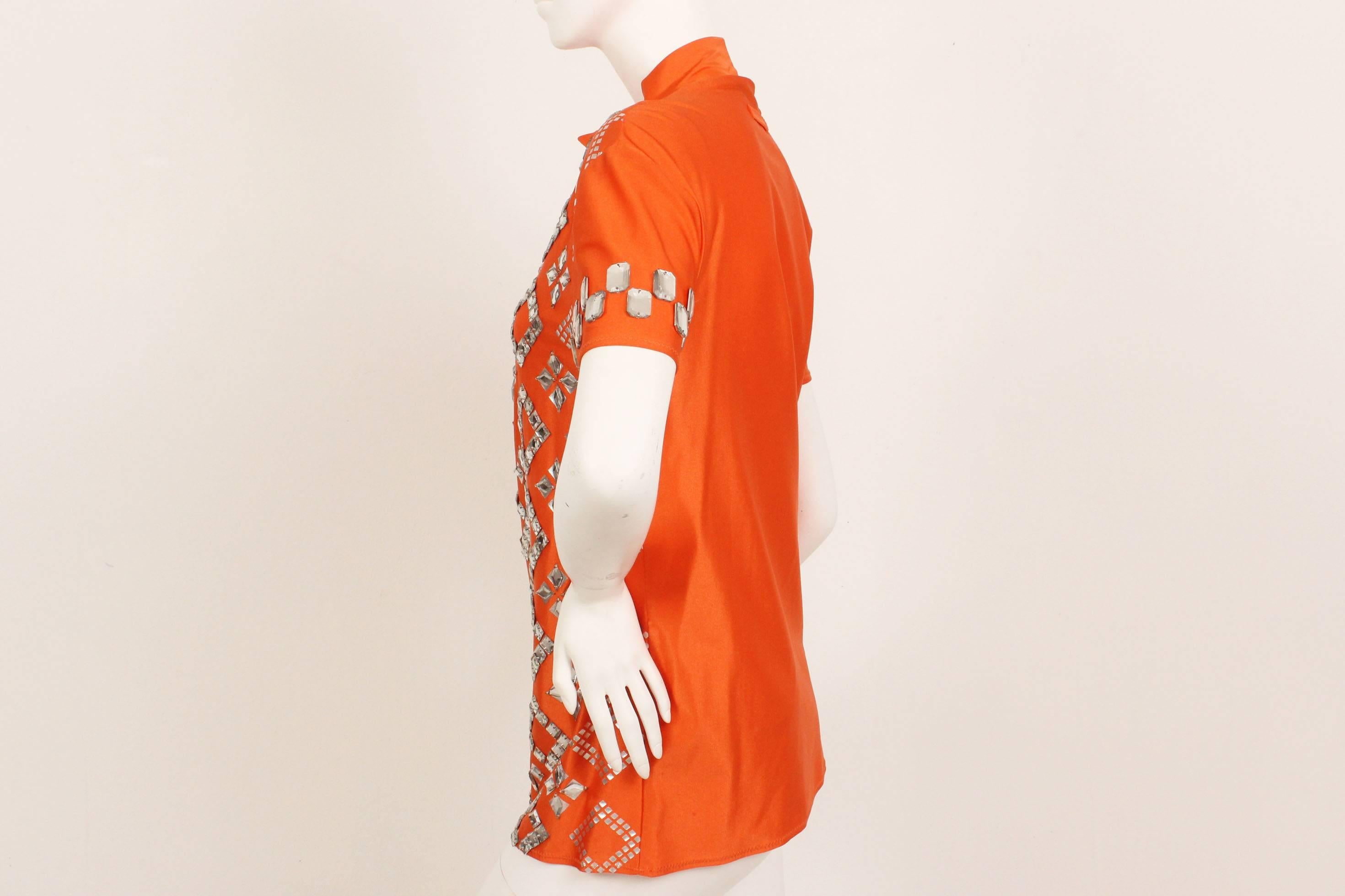 This Jean Paul Gaultier pour Equator piece is all about sporty glamour. The vibrant tangerine orange color of this short sleeve mock neck is shimmery and playful. Plexi mirrored gems adorn the front with metallic silver grids in geometric shapes and