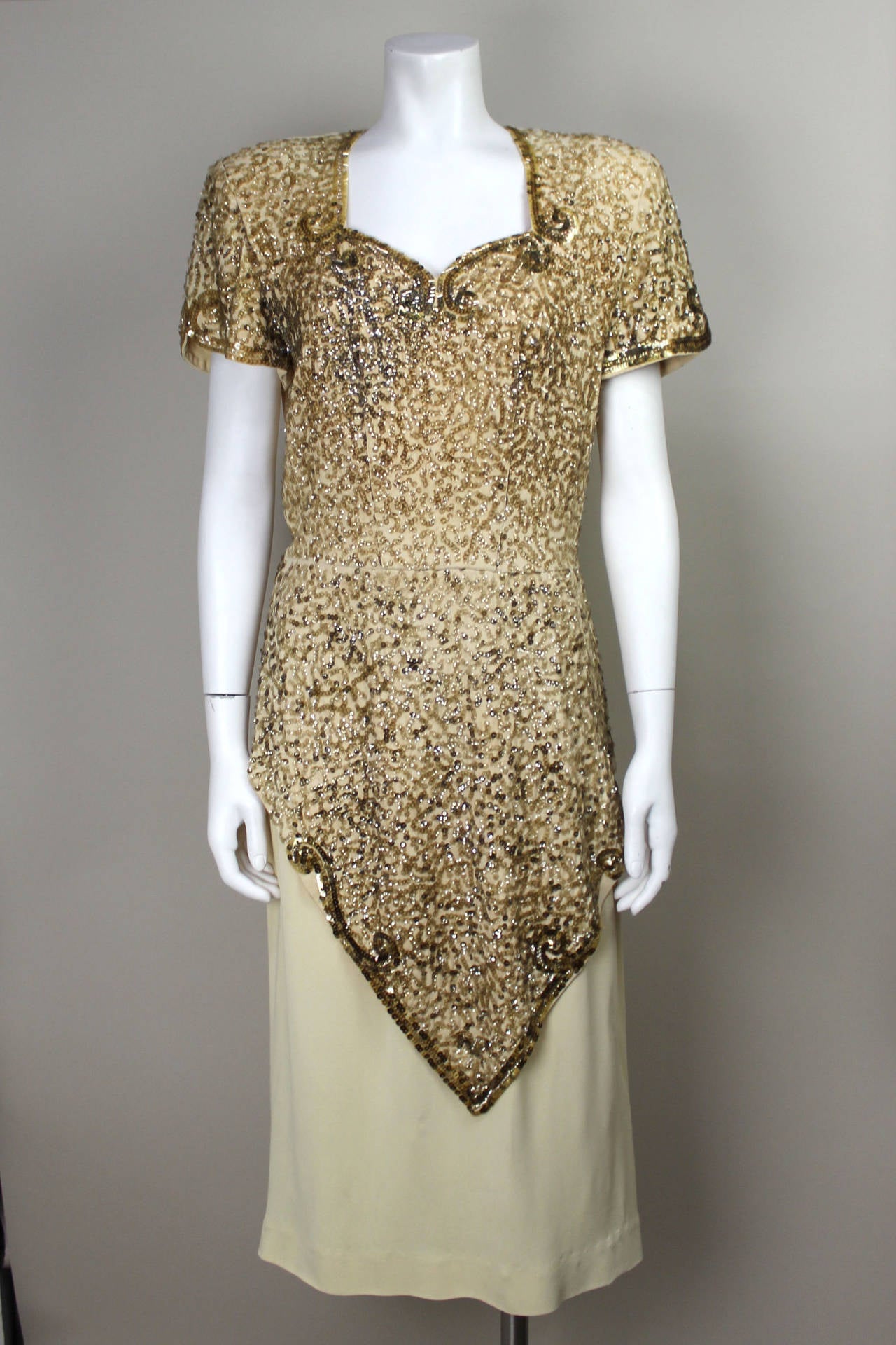 This creme rayon dress is embellished with an intricate design of hand stitched gold sequins. The style is pure 1940's glamour. The sleeves, sweetheart neckline, and front are all sequined ending in a draped overlay. A belt in the same creme rayon