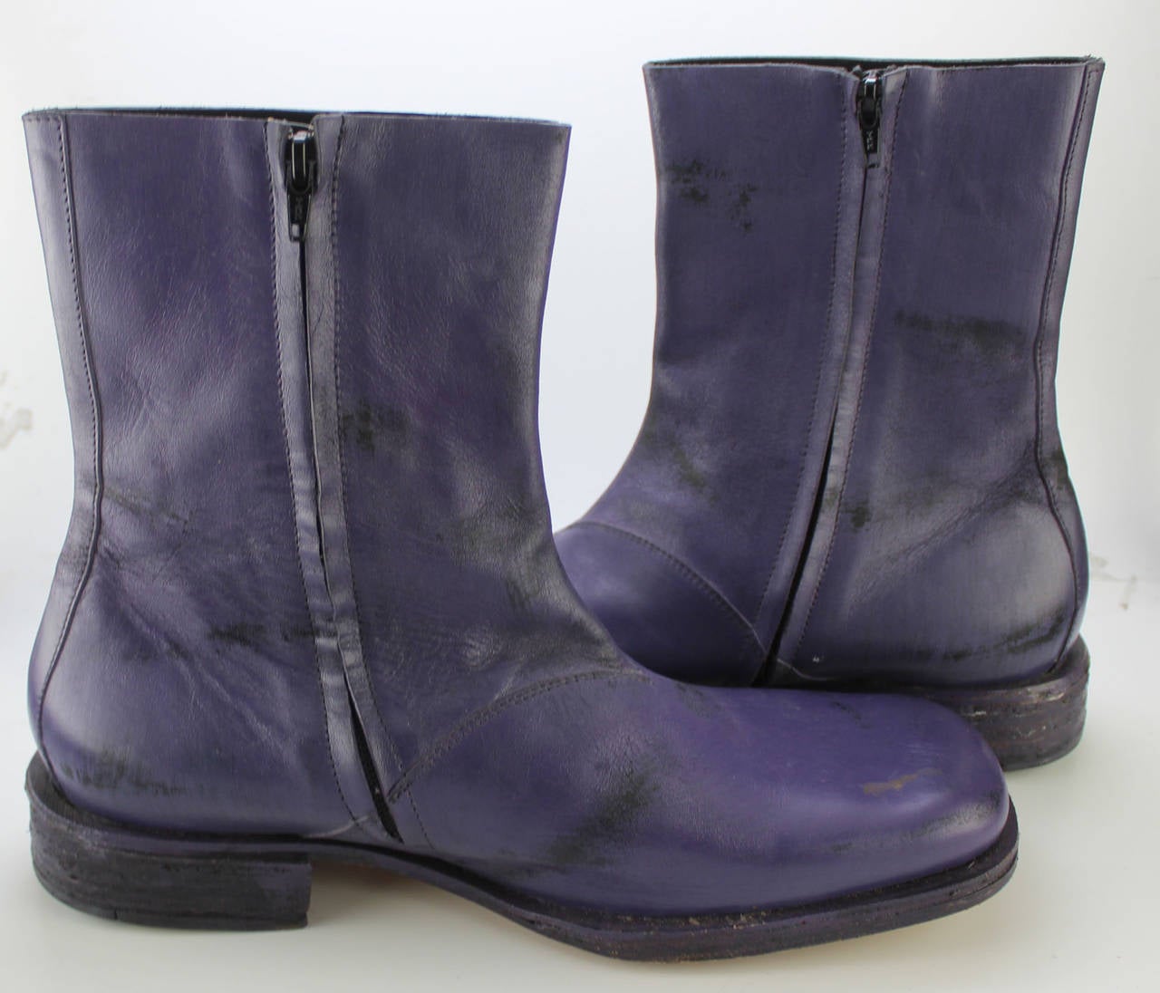 These boots were produced early on during Martin Margiela's designing years. They have his signature distressed leather painting. This particular pair has black over a dark purple. They have a square toe, side zipper, and a 1 1/2 inch rugged heel.