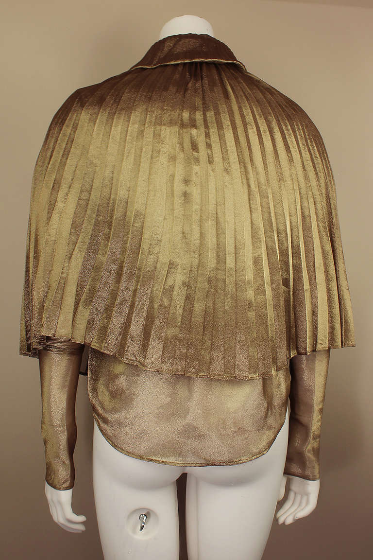 This is a stunning button down blouse with an accordion pleated collar and attached capelet. It has extra long narrow sleeves to be pushed up in gathers. The body is a sheer metallic.