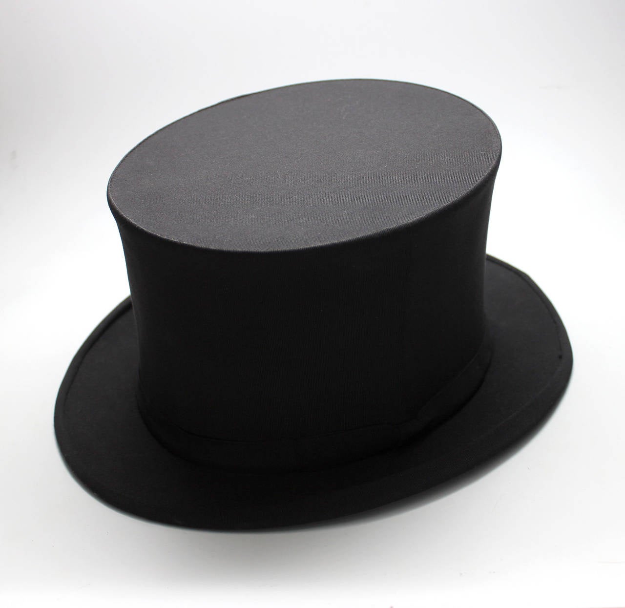This collapsable top hat is in excellent condition with a hidden spring mechanism that works perfectly. The hat is covered in an elegant black satin grosrain with a matching narrow ribbon around the outer band with a simple flat black bow on one
