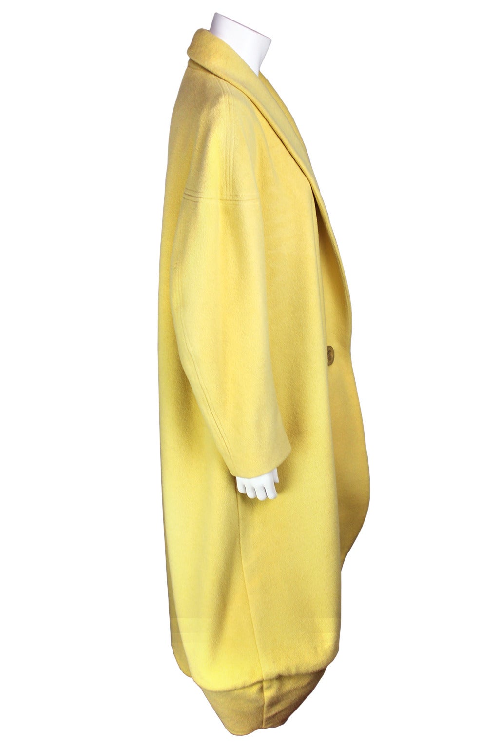 This stunning garment is a fine example of John Galliano's early designs. The wool is in a soft butter hue. It has a wide shawl collar which closes in a single button. The hem is cleverly constructed with a seamed cocoon shape. This is a wonderful