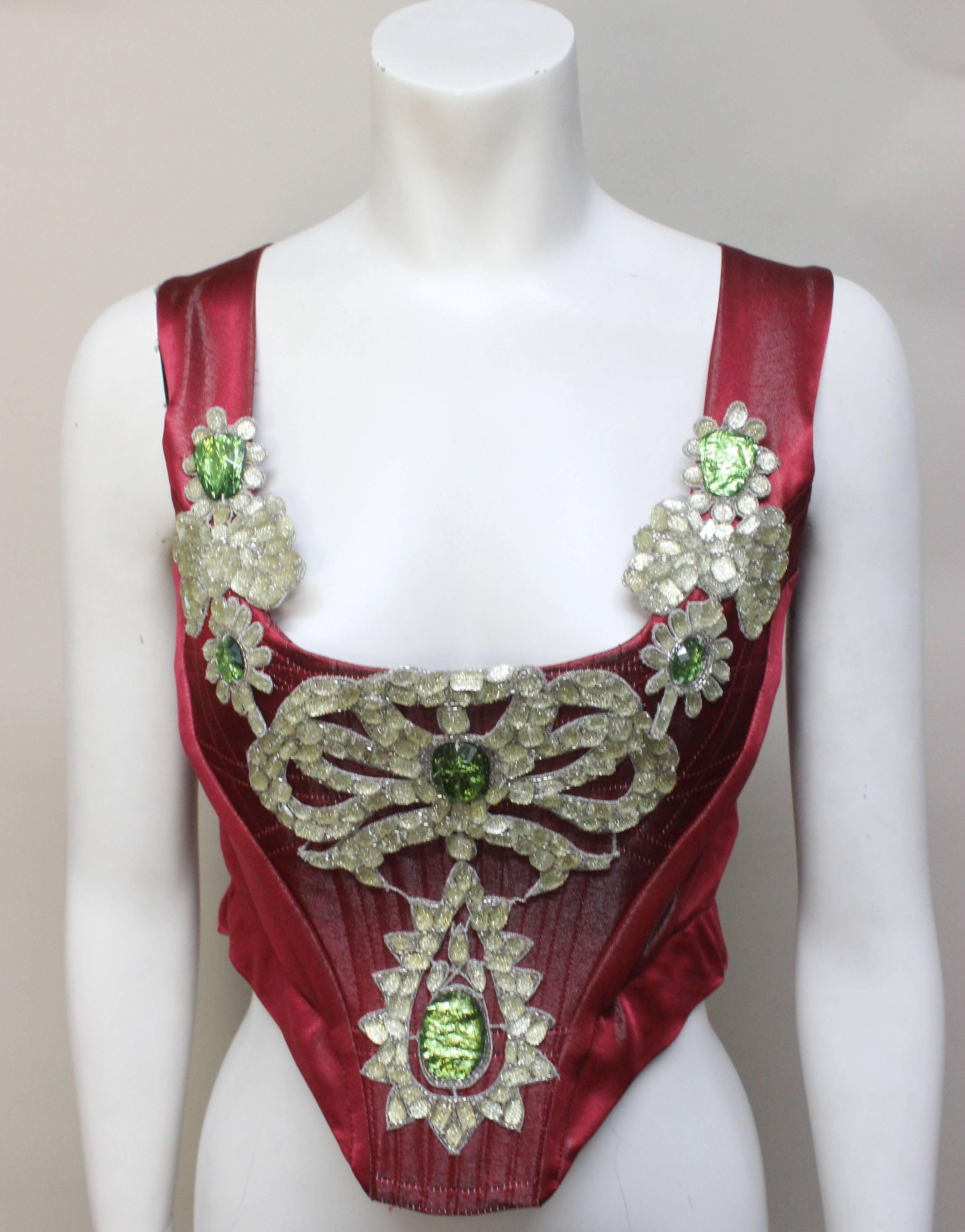 This never worn bejeweled deep scoop neck corset is a delicate and beautiful piece, perfect for the holidays. The front and back are boned, and the front has a light and dark green jewel design on top of the beautiful deep red silk blend. This