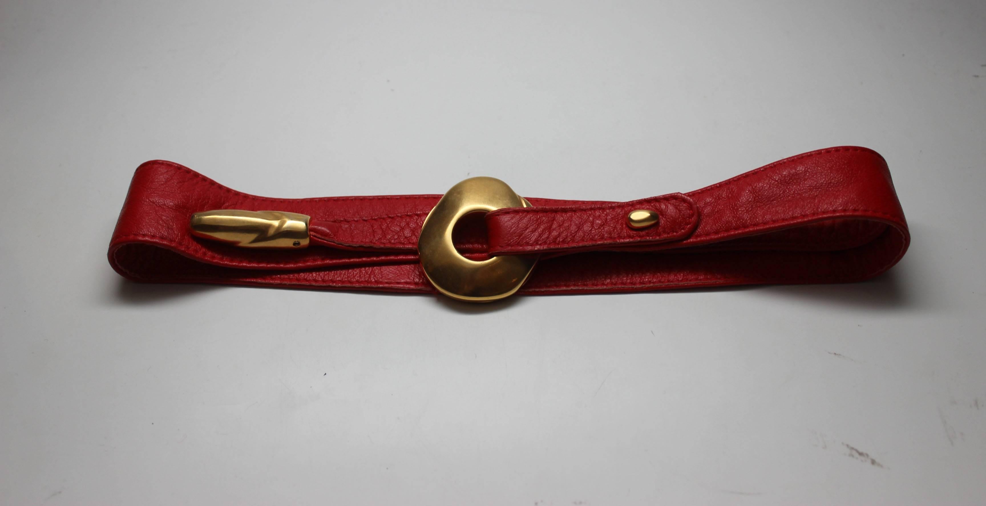 Donna Karan's accesories often have unique sculptural details. This vibrant red leather belt closes by looping one end through a gold orb, which then wraps around the belt. The end is encased in another bit of gold hardware. This belt can be worn