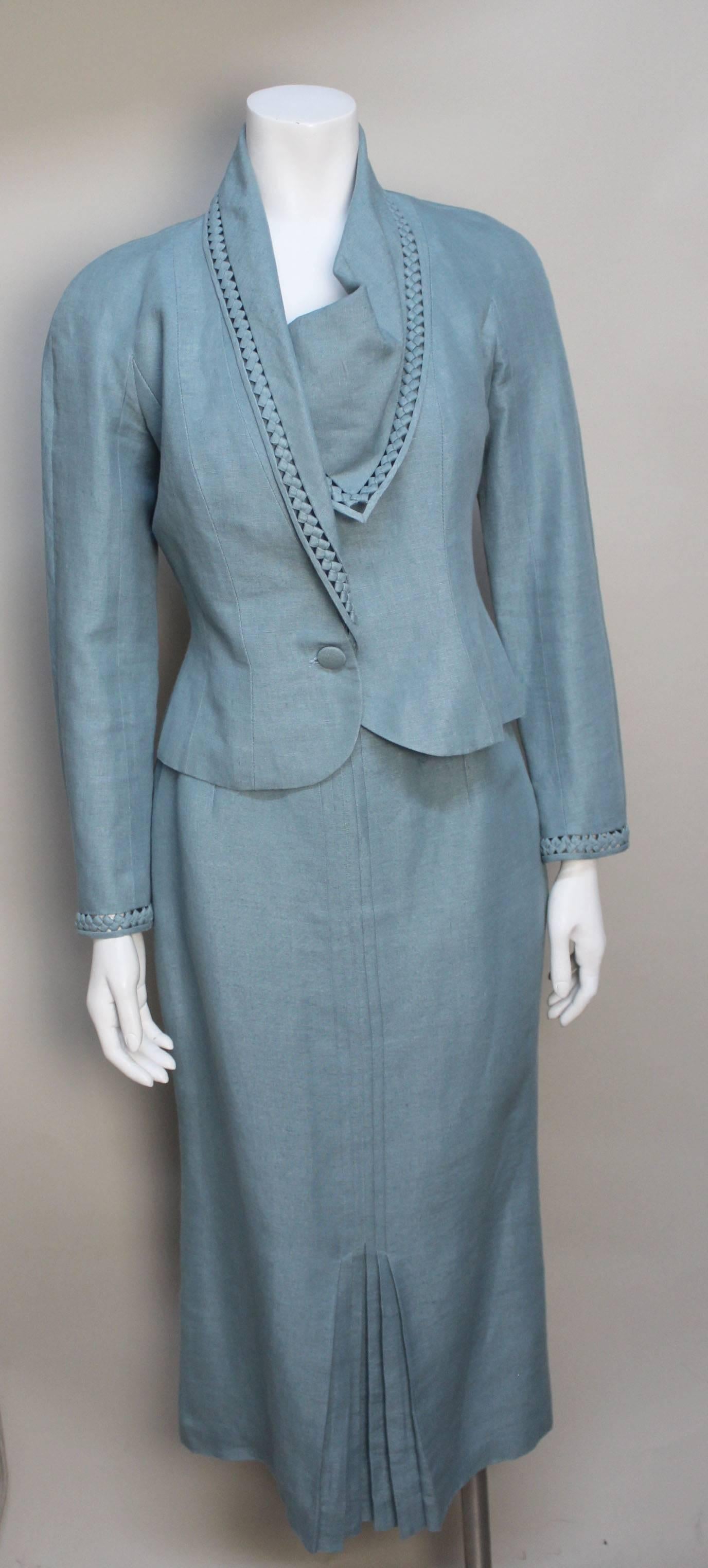 This womans two piece suit with skirt has many wonderful details. The suit is made of a fine slate blue linen completely lined in silk. The fitted skirt ends mid-calf with a kick pleated front. The jacket drapes beautifully with an asymmetrical