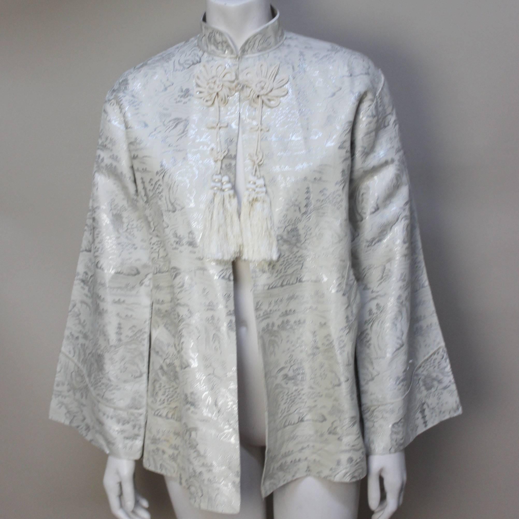 This is a gorgeous 1940's jacket with knotted florets, tassels and a silver on ivory design of a Chinese landscape. It has a classic mandarin style collar with a fastening at the neck and is completely lined. The silouette is slightly a-line with