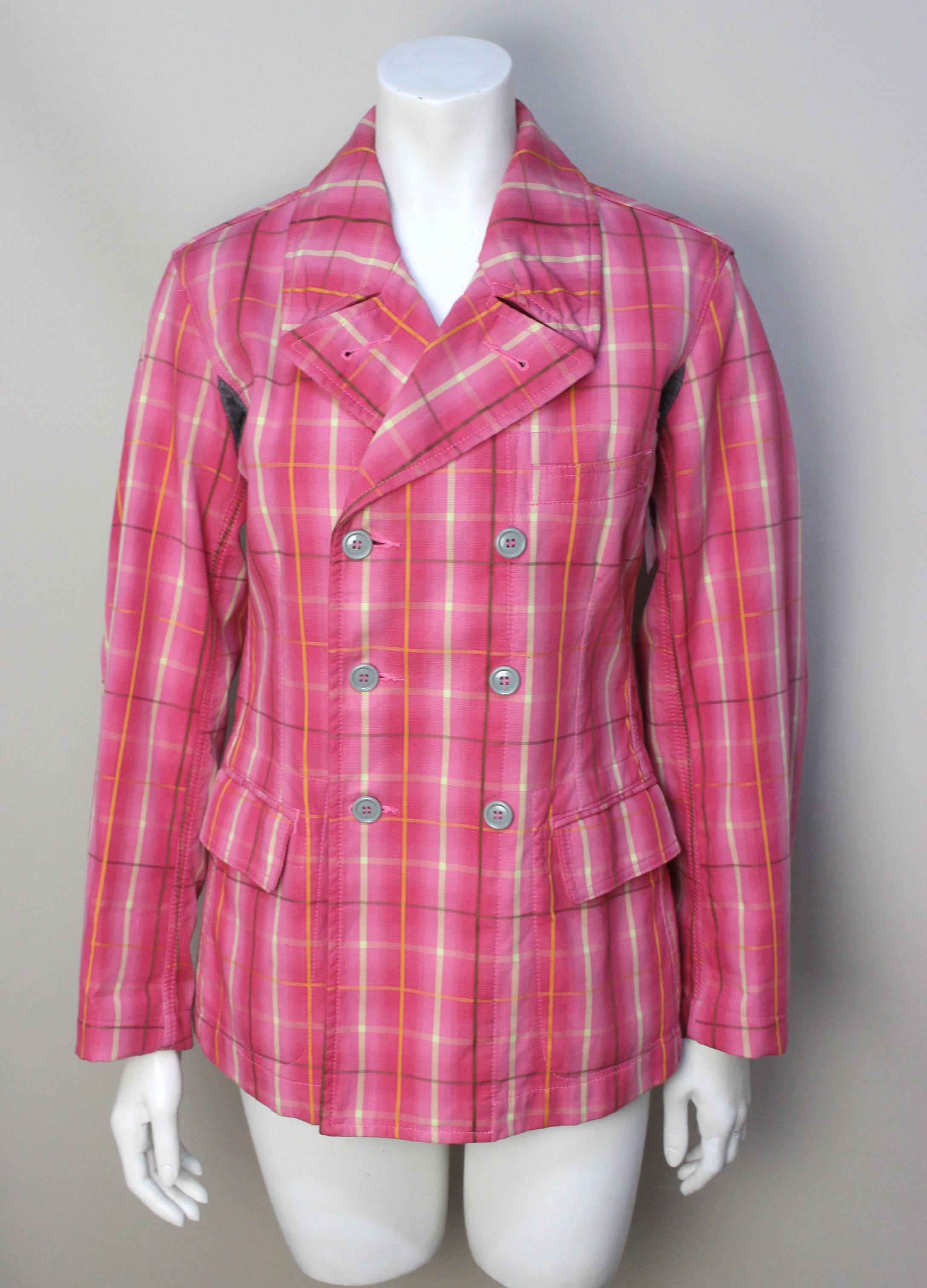This vibrant pink plaid jacket has a quirky detail of grey wool armpit inserts that tags it as a Comme Des Garcons design. The body is fitted and double breasted. The bright cotton plaid fabric is lined in an earth tone corduroy, another eccentric