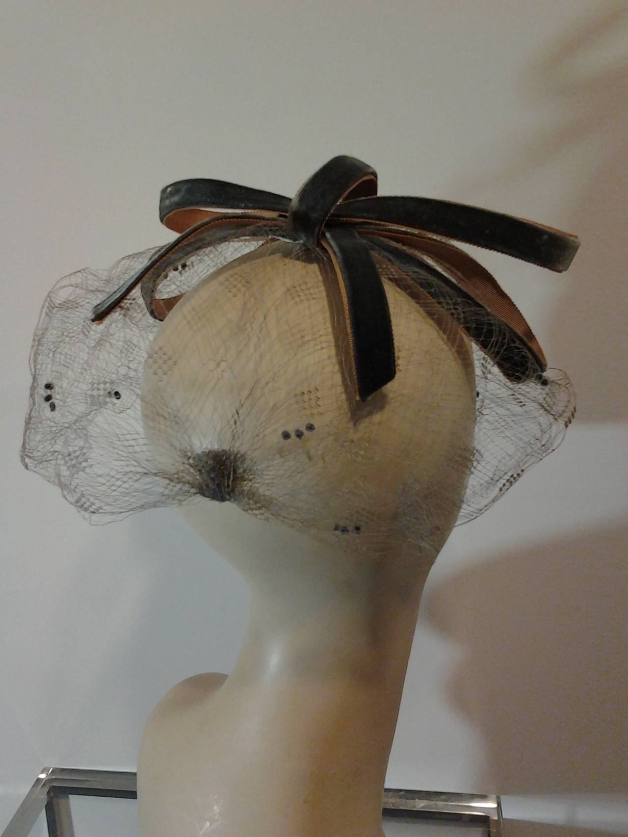 A beautiful 1960s Vidal veiled fascinator hat of stiffened sage green-gray velvet ribbon fashioned in a multi-looped bow with patterned veil
