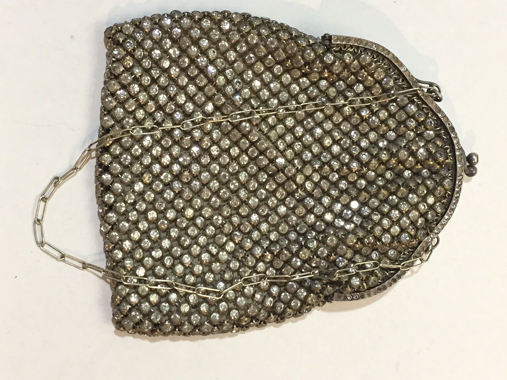 A gorgeous 1920s Art Deco metal mesh evening bag completely covered in bezel-set rhinestones.  Original lining in good but slightly marked condition. 

Small stones missing on metal frame and clasp, but all present on mesh. 

Chain handle is 14