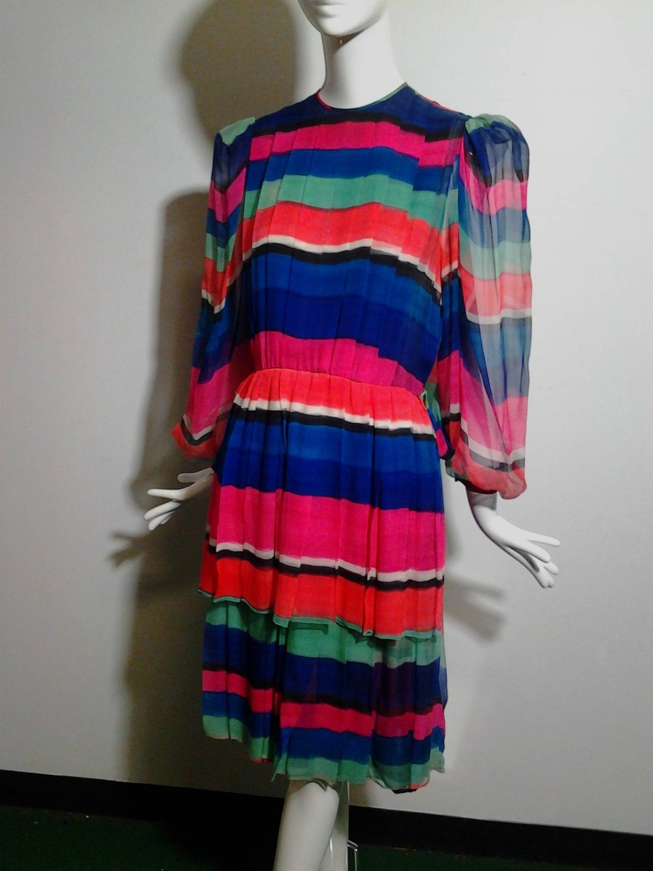 A strikingly colored, striped James Galanos 1980s pleated silk chiffon cocktail dress with two-tiered skirt, sheer puffed sleeves, and full blouson back panel.  

Separate Galanos lime green leather belt can be included.