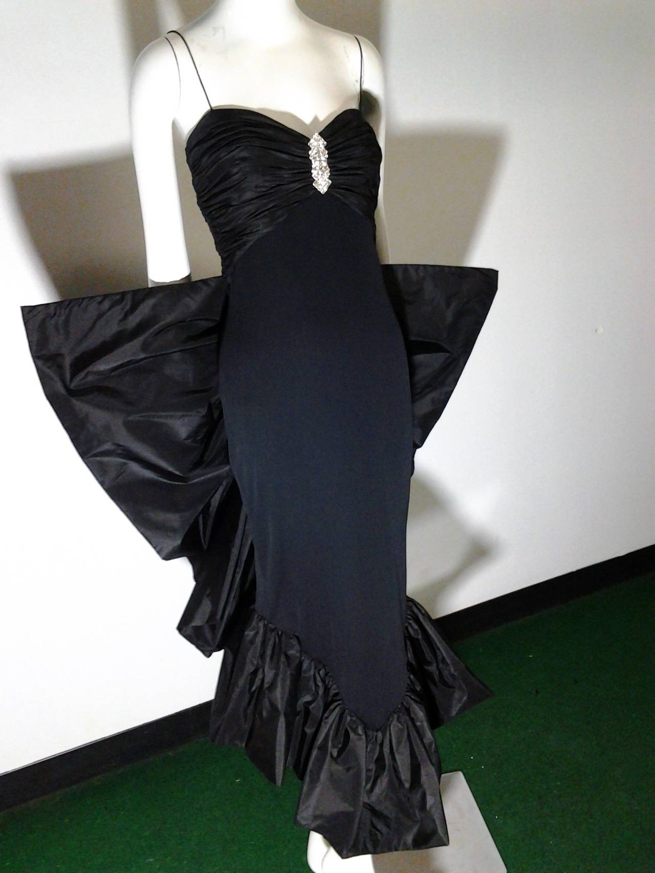 1980s Jill Richards dramatic black matter jersey cocktail dress:  Spaghetti straps, ruched bodice , rhinestone décolletage embellishment and a large silk taffeta fan shaped ruffled bustle at back. Back zipper.