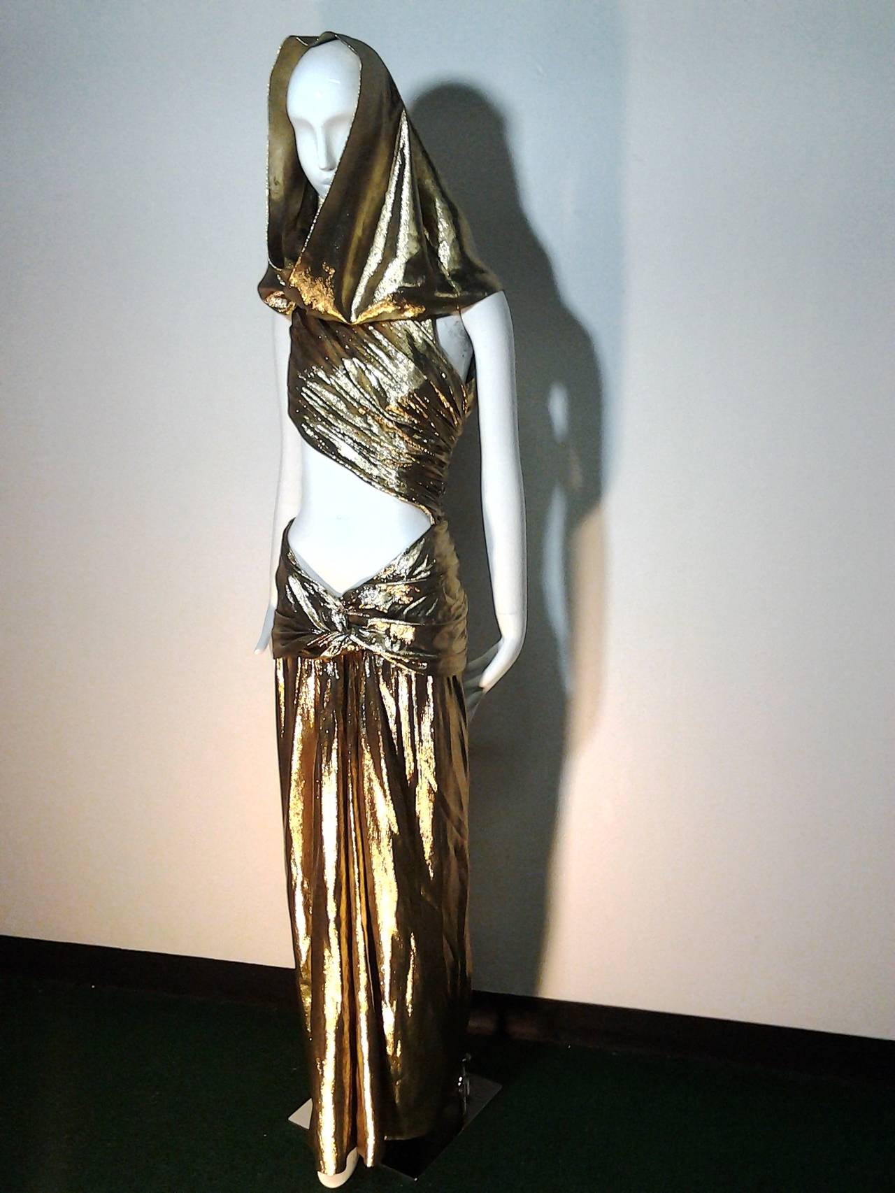 Iconic Yves Saint Laurent, Long evening dress, with 90's waist cut-out and draping.
Rive Gauche collection, Fall-Winter 1991.
Draped gold lamé with hood and daring cut-out midriff.

In the permanent collection of the Denver Art Museum. Featured in