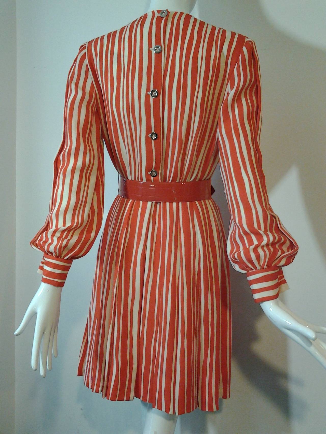 A sexy 1980s James Galanos orange and cream chalk stripe day dress:  Buttons down back. Zipper at back of skirt.  Skirt is lined and full with box pleats around entire waist. Front and back center vents.  Balloon cuffs.  Belt included, but not