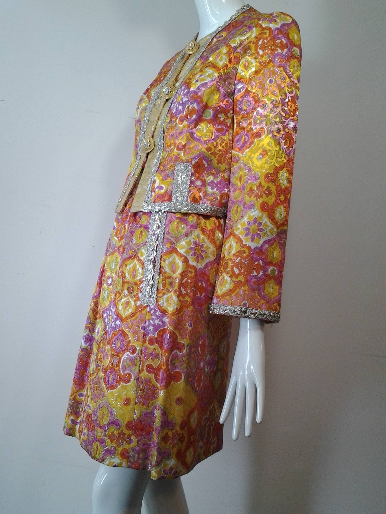 1960s Fern Violette lame floral brocade cocktail suit w/ metallic braid trim and large jeweled buttons at front and cuffs. Silk lined. Pockets at skirt front.