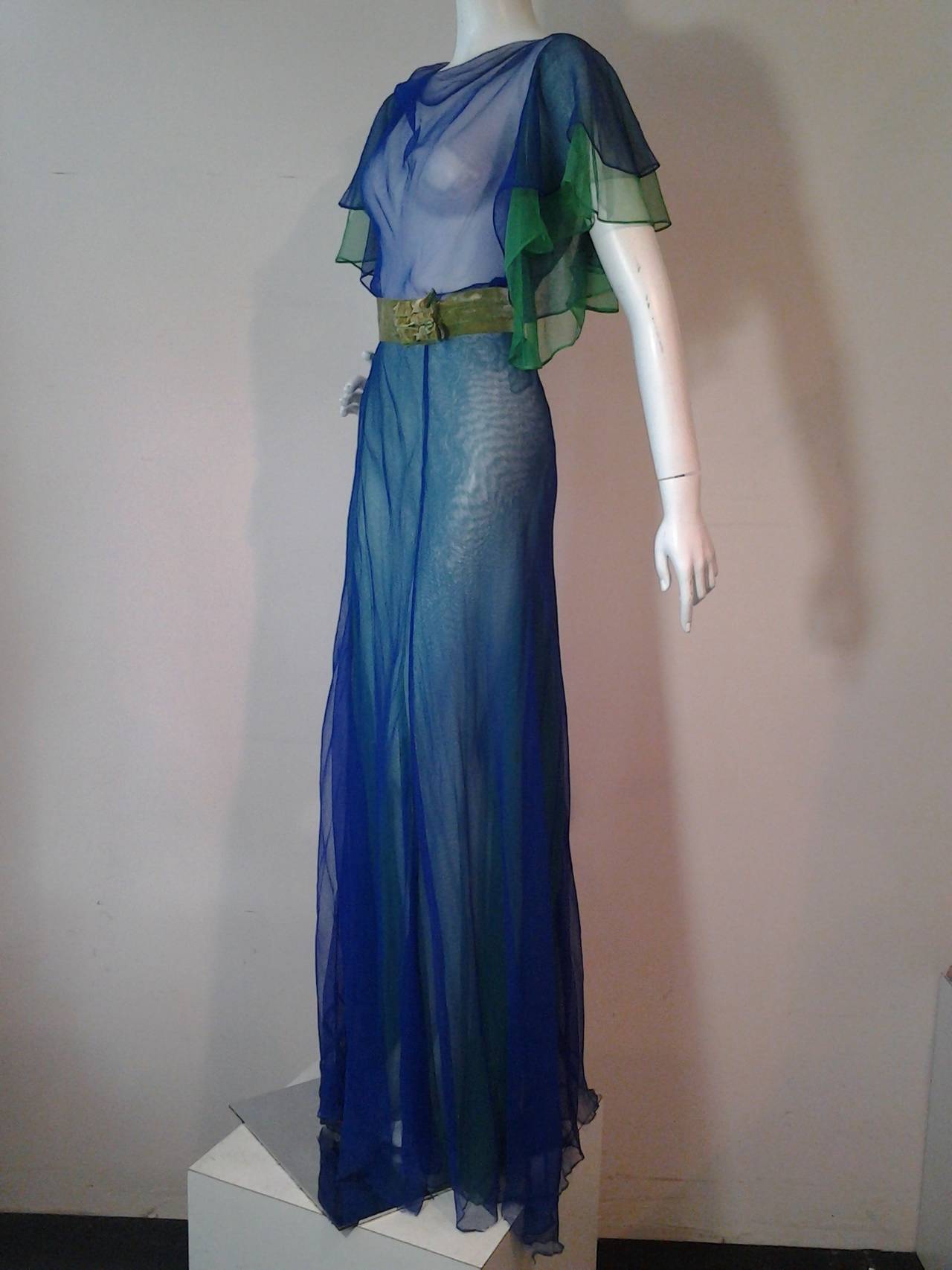 A vivid, bold 1930s silk chiffon gown in layers of cobalt and kelly green.  Bias-cut, slightly cowled neckline in front and plunging in back. Extravagant ruffled cap sleeves. Side snap, hook and eye closures.  Original velvet 2.5