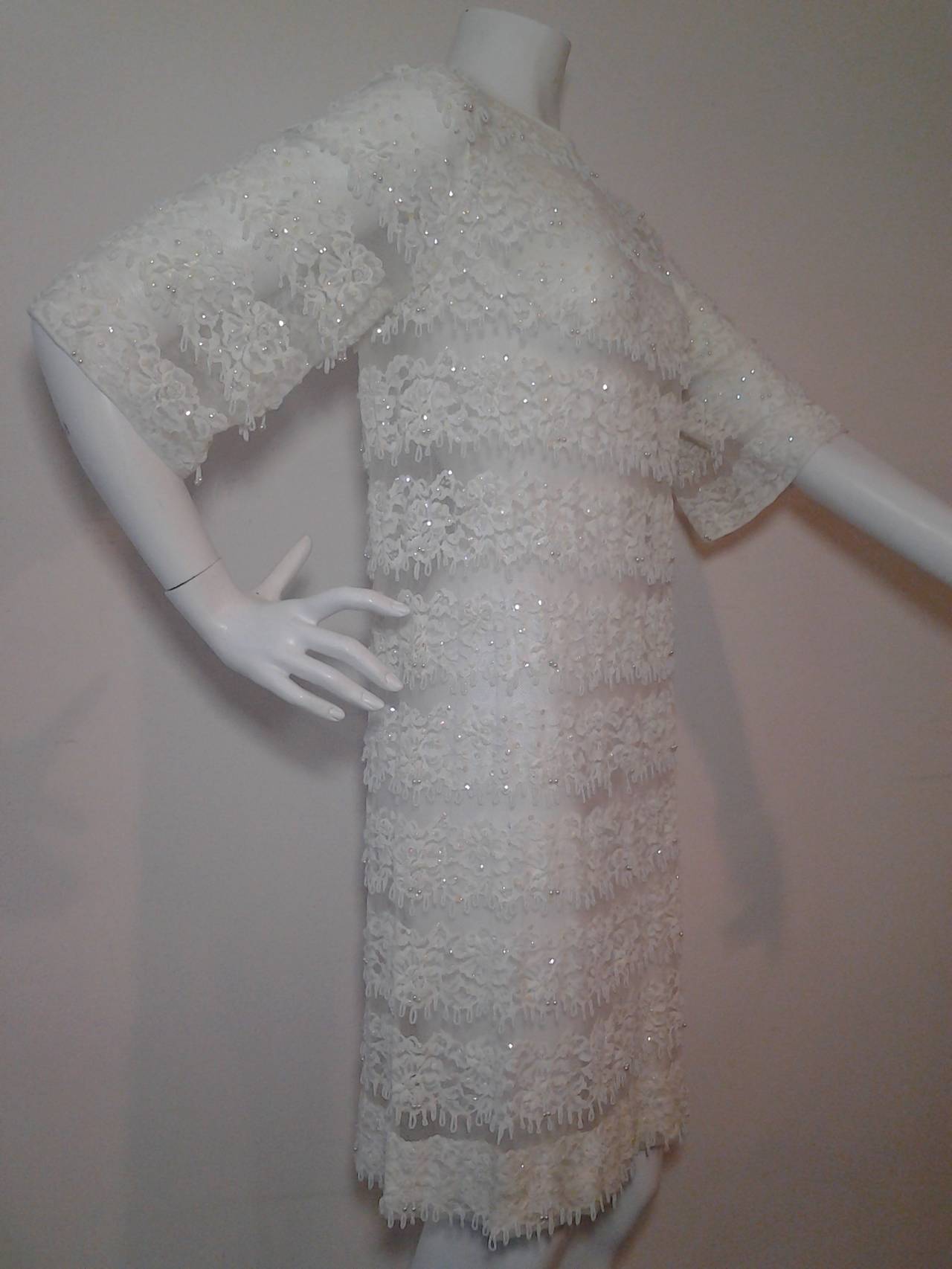 1960s white net lace cocktail mini dress w/ beaded and sequined banding. Sheer with no lining.  Hem is stiffened and weighty.   Hook and eye back closure.