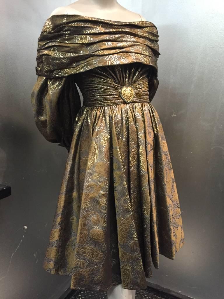 A 1980s Michael Casey pewter, gold and copper metallic brocade paisley patterned cocktail dress with balloon sleeves, large folded back button cuffs, full gathered knee-length skirt, a pleated and draped, back-dipping portrait collar and a gathered