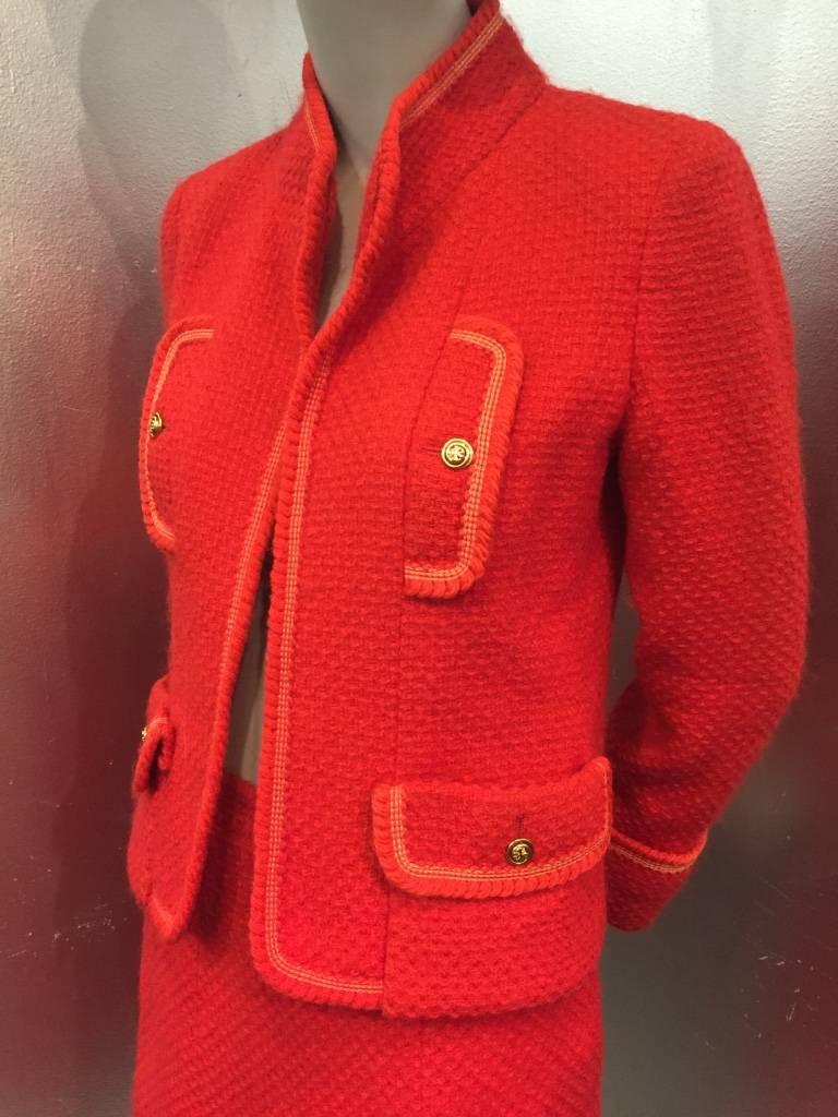 A gorgeous 1980s cardinal red Chanel Boutique wool tweed skirt suit with braid trim at collar pockets and cuffs, shamrock motif metal buttons and signature chain sewn into jacket hem as weight.  Fully lined. 