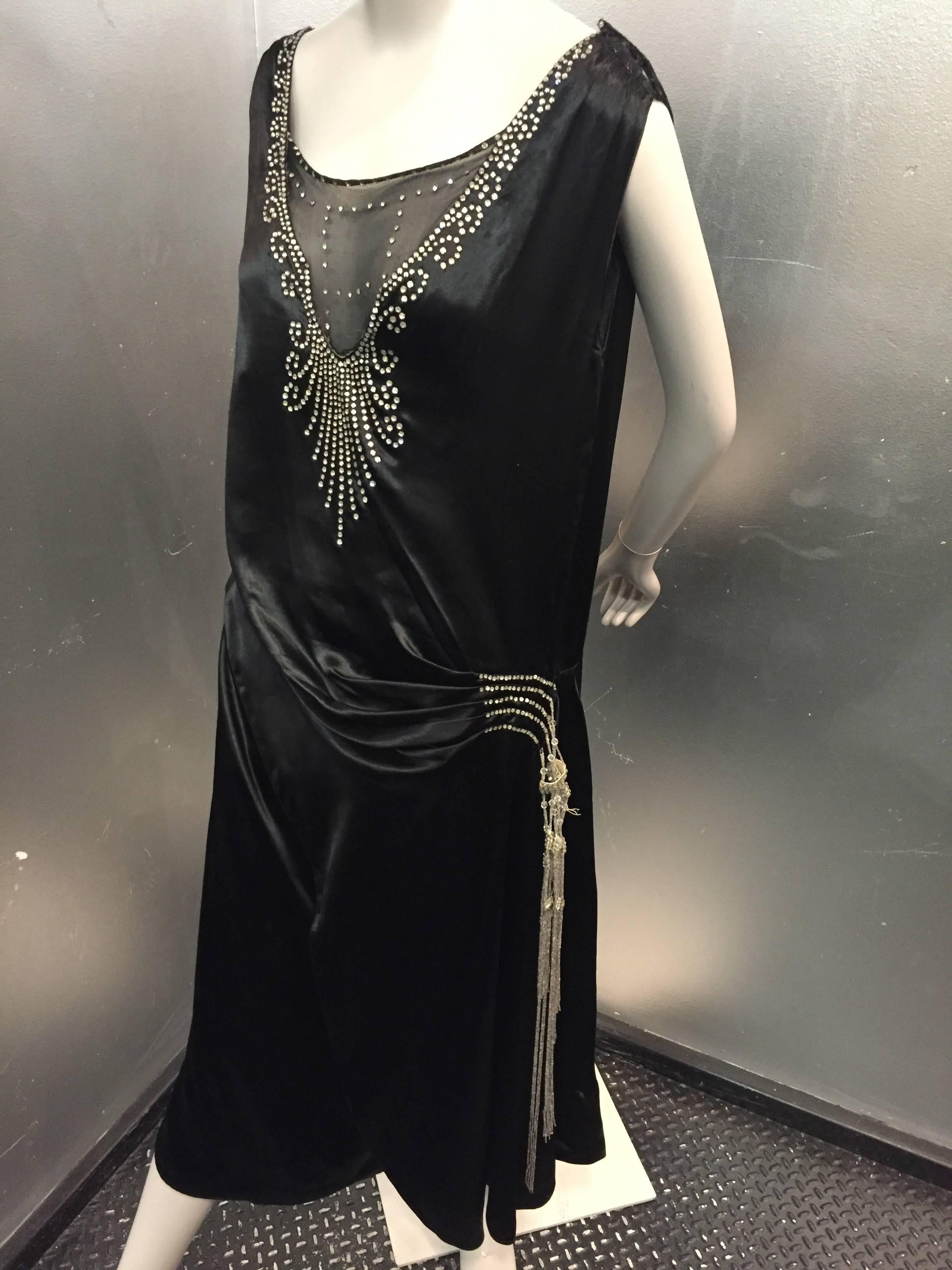 1920s Art Deco black silk satin Gatsby-style evening dress: Sheer chiffon panel at décolletage with elaborate beading and studded with rhinestones.  Drop-waist is draped to one side with heavy bead tassels. 