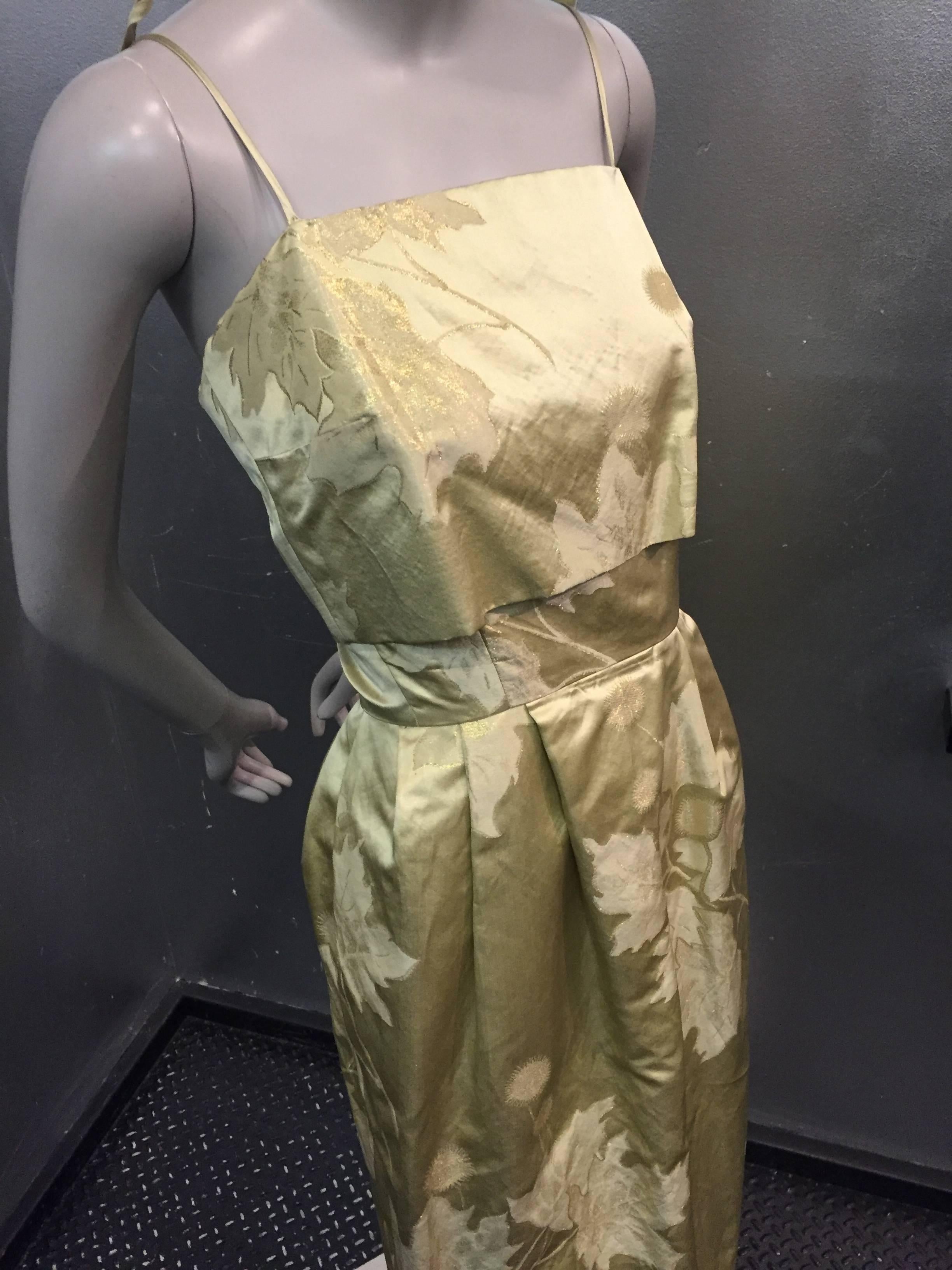 A gorgeous 1960s gold silk jacquard leaf-patterned evening gown with fitted waist, spaghetti straps, a slight pouf at hip and tapered to hem.  Bodice has an over-panel that floats over fitted layer. 