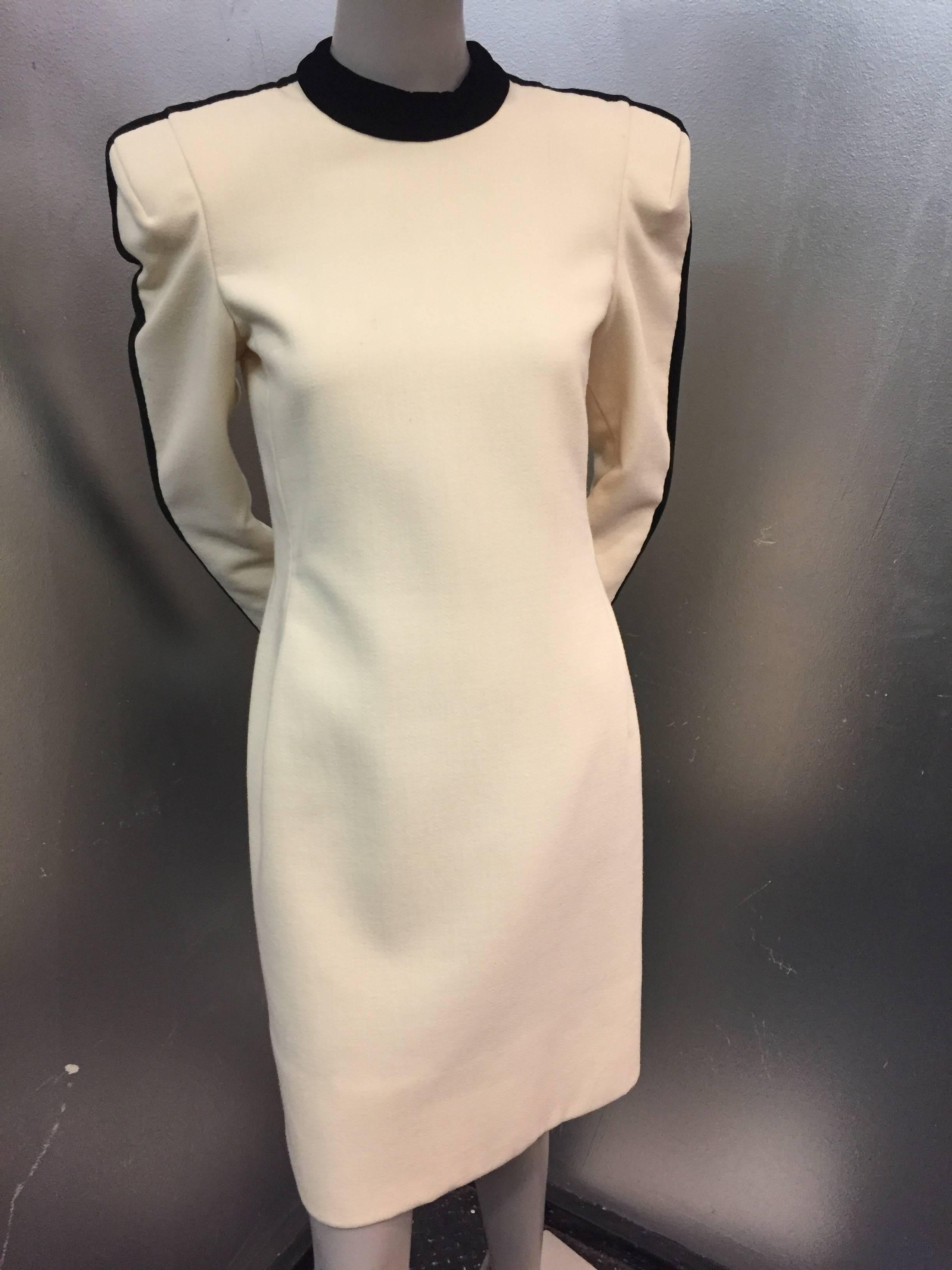 A very structural cocktail dress in cream wool crepe features bold shoulders trimmed in black velvet at sleeve and neck.

Fully lined and zipper at back and at cuff.

