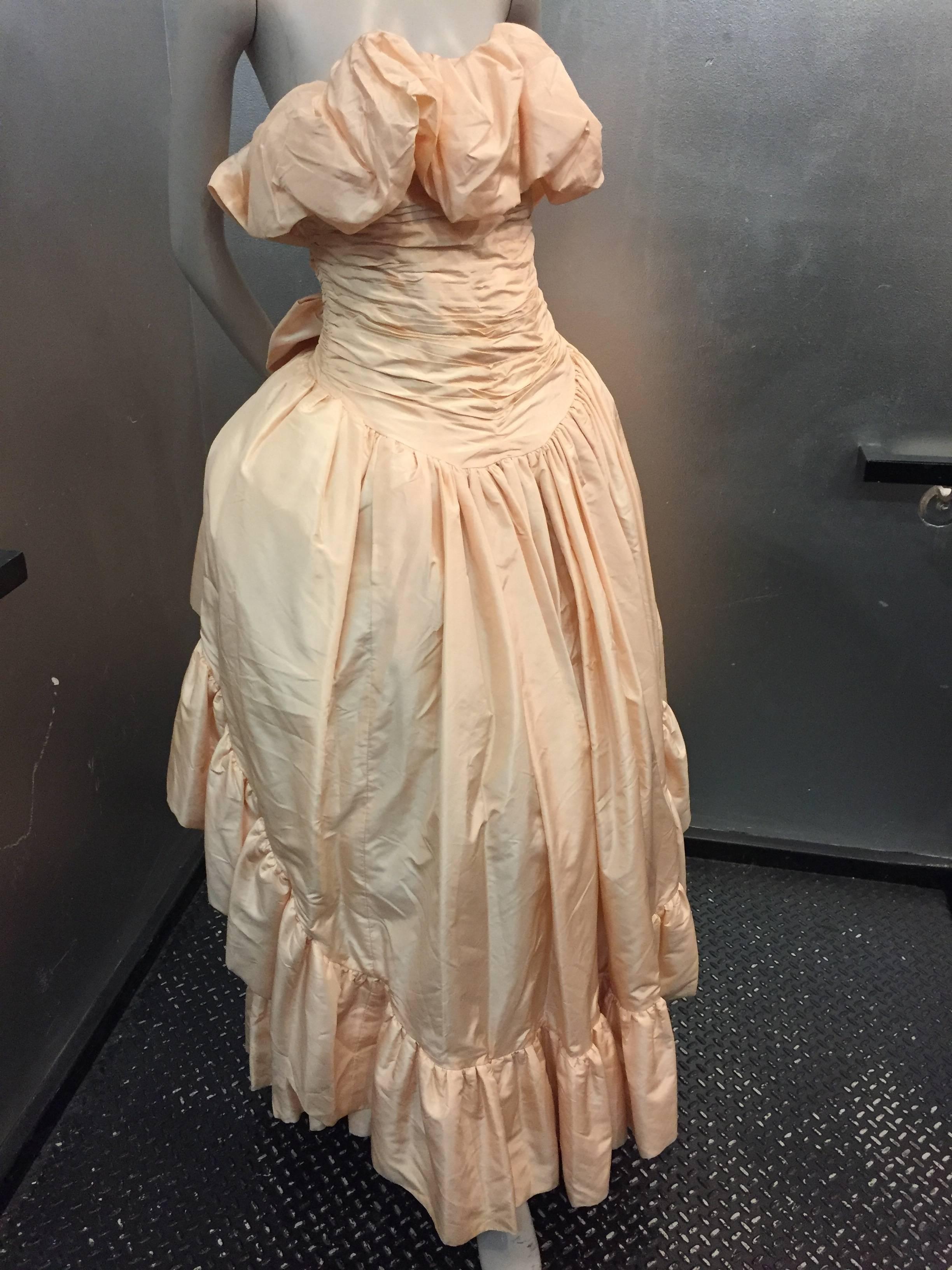 1980s Arnold Scaasi shell-pink tissue silk strapless ruffled ball gown with back bow. Very full skirt with gathered tulle crinoline under each tier of skirt. 