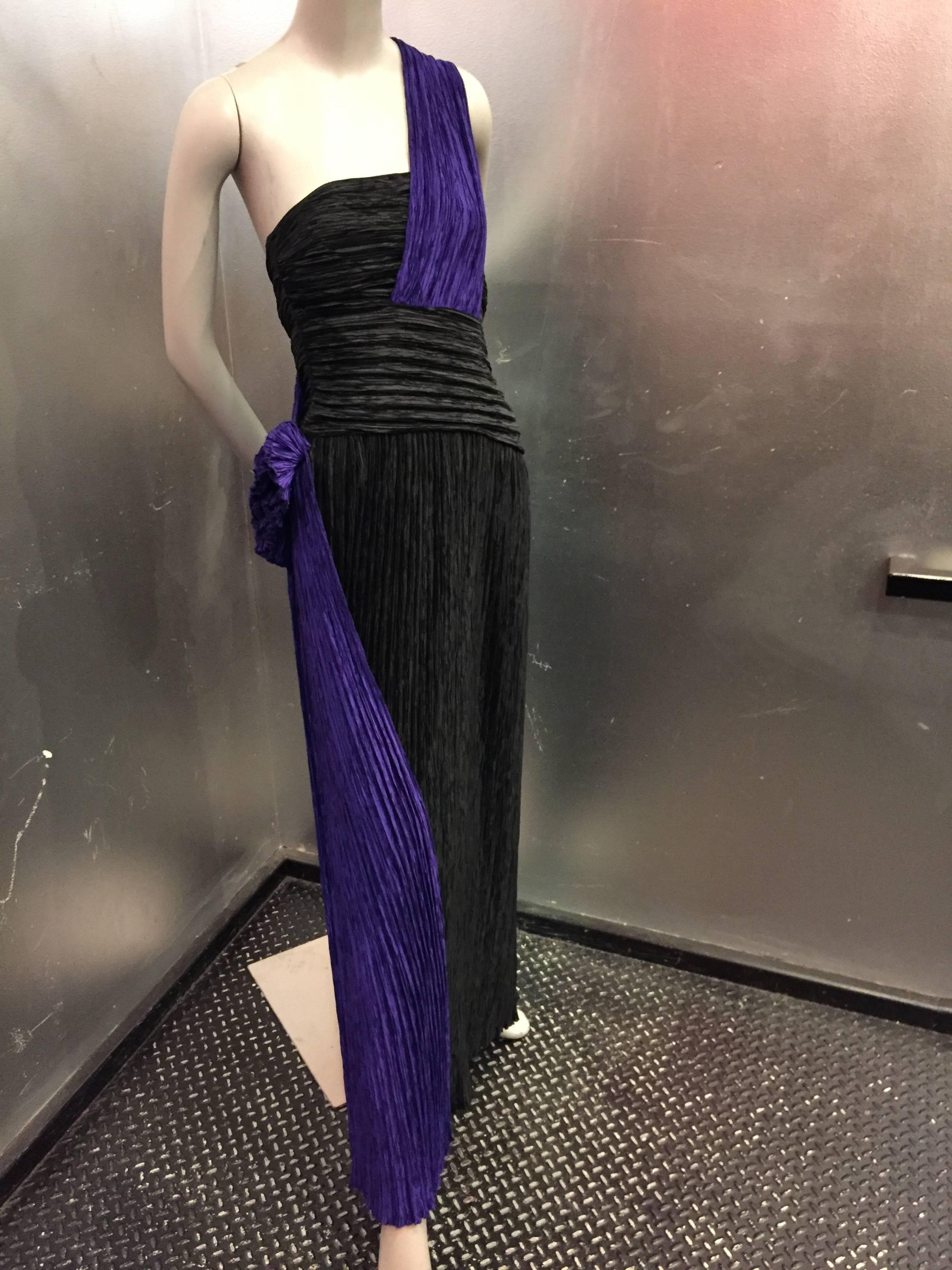 A strikingly modern two-tone purple and black Fortuny goddess gown with one-shoulder draping, reminiscent of a sash that ends in a side swag. Boned bodice with a side zipper. 

Fits a modern US size 8. 