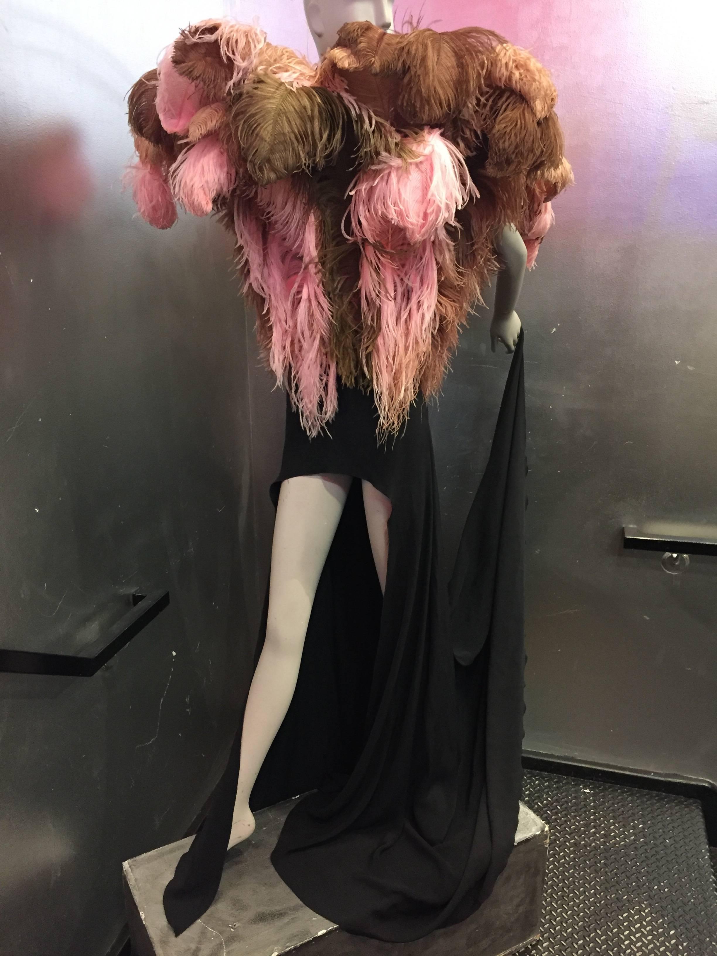 An astounding 1980s Tilmann Grawe avant garde black crepe gown with high hem in front and long train in back.  Front waist to décolletage, around entire gown is a fountain of pink, brown and tan full and lush ostrich plumes attached st a faux