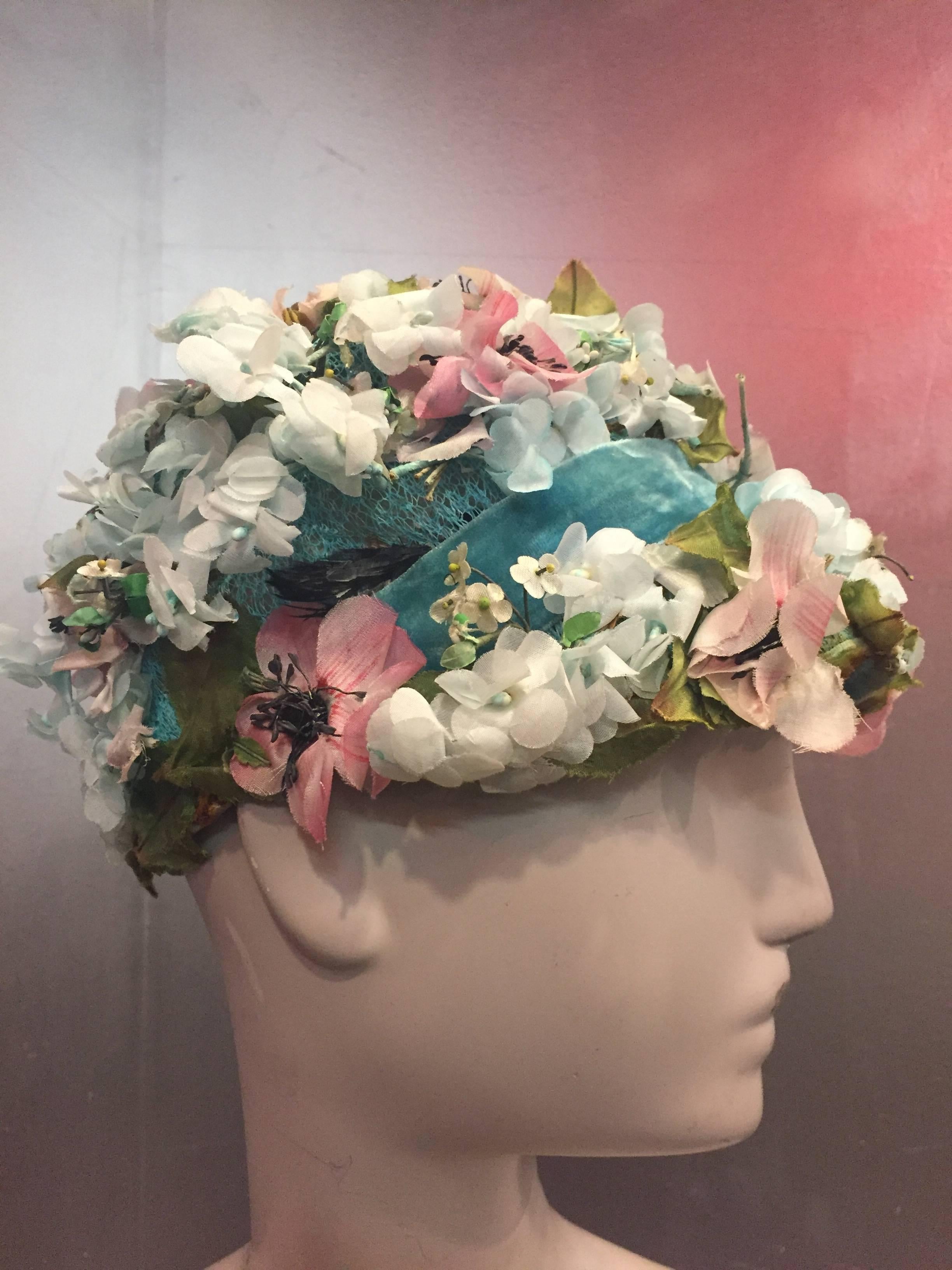 This is a fabulously constructed green net hat, banded in green velvet with a profusion of small, medium and large white silk flowers. To add to the intricacy, each flower type has a different colored stamen. This adds little dots of white, blush,