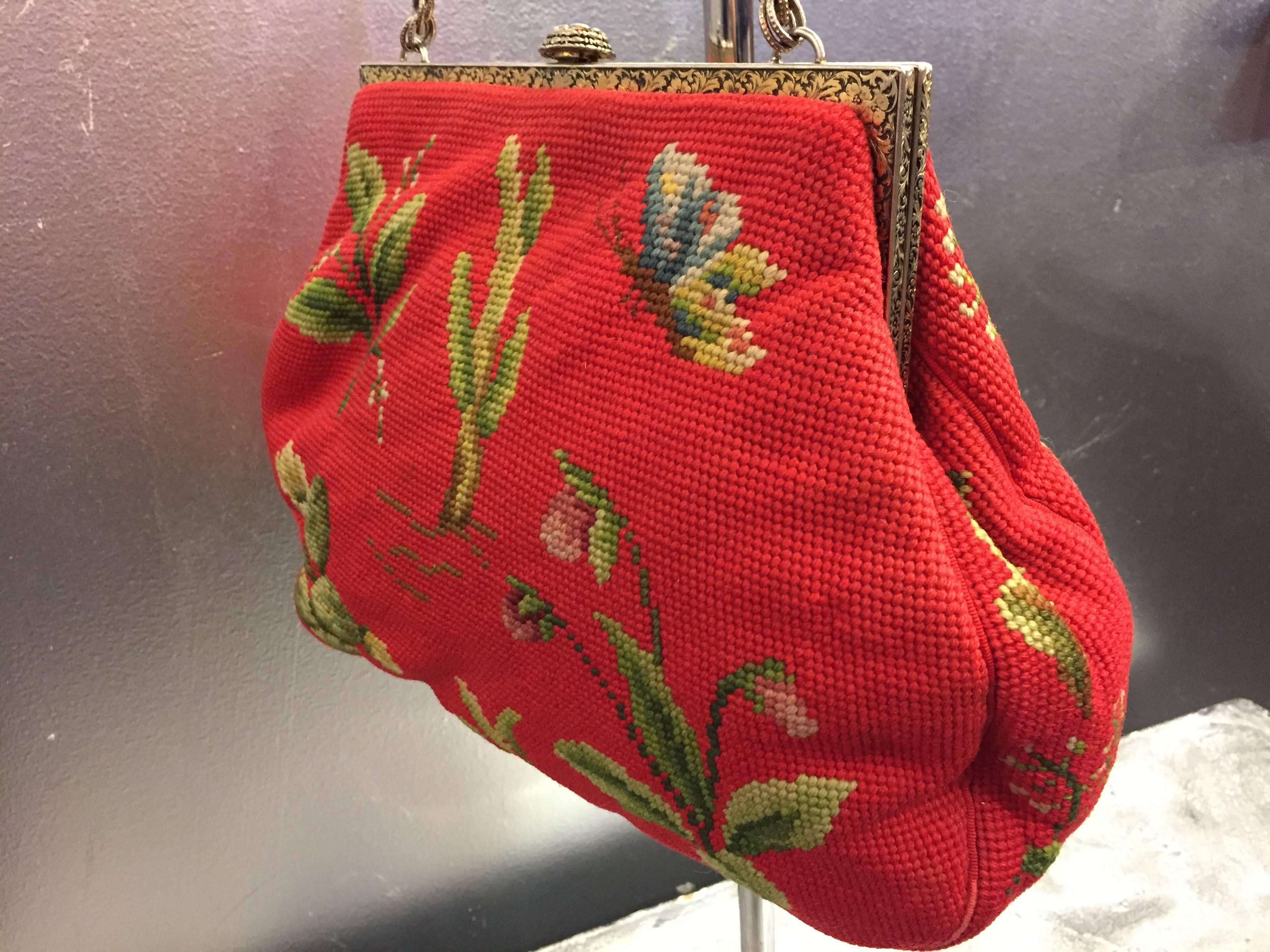 A fantastic and rare extra-large needlepoint purse from Maud Hundley in a lovely botanic pattern featuring butterflies, ladybugs, flowers and leaves. The frame features a floral scroll pattern in brass with a rosette clasp and chain handle. The