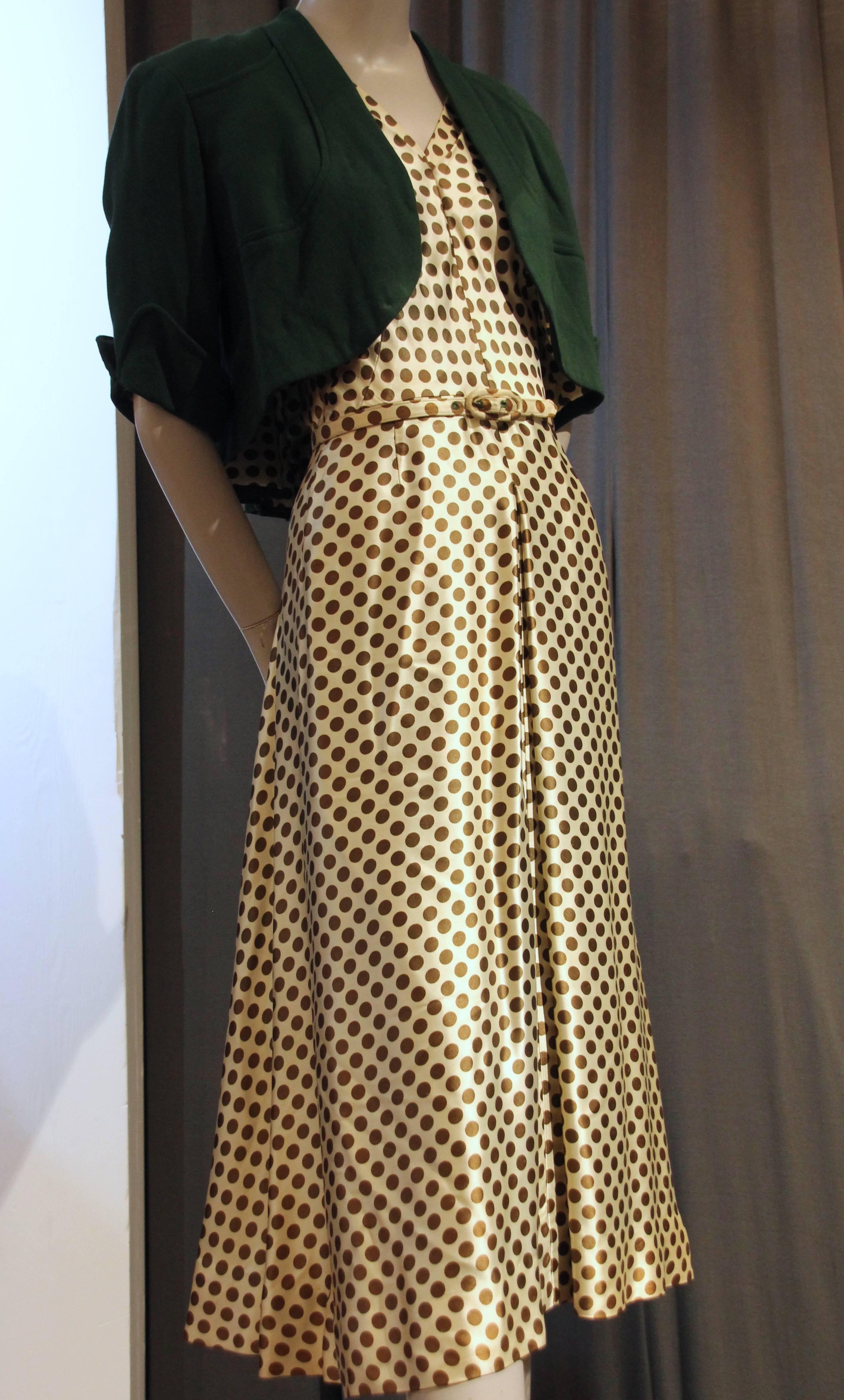 A charming 1940s coordinating ensemble--sold together:  A green and cream polka-dot silk satin dress with flowing skirt and tailored bodice, with a lightweight green wool jacket.  Full swing weighted back and short cuffed sleeves in a bolero style. 