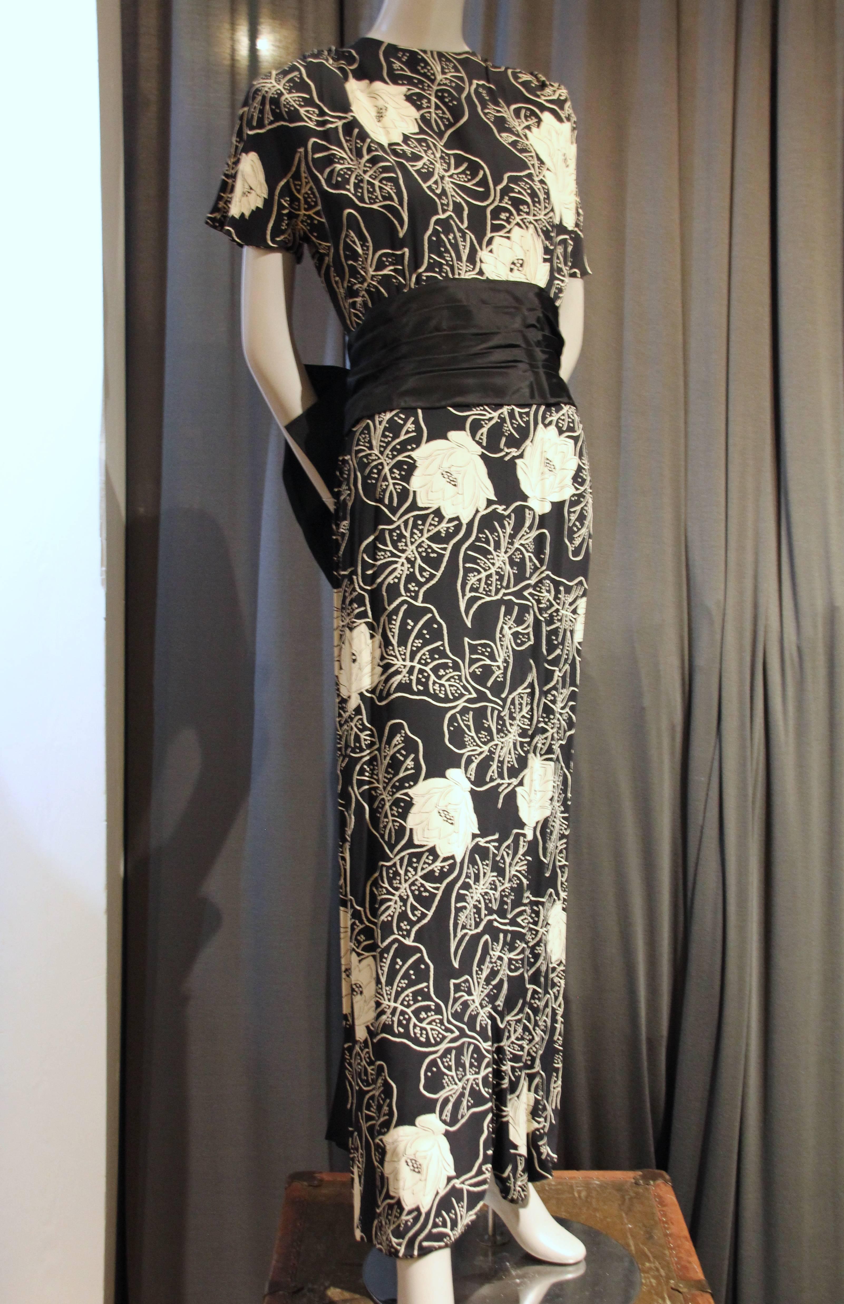 A beautiful 1940s Eisenberg Original black and white floral print gown in flowing rayon:  Classic 1940s styling with shoulder pads, simple rounded collar, draped bodice and fitted hip.  A neat column silhouette is adored with a black silk taffeta