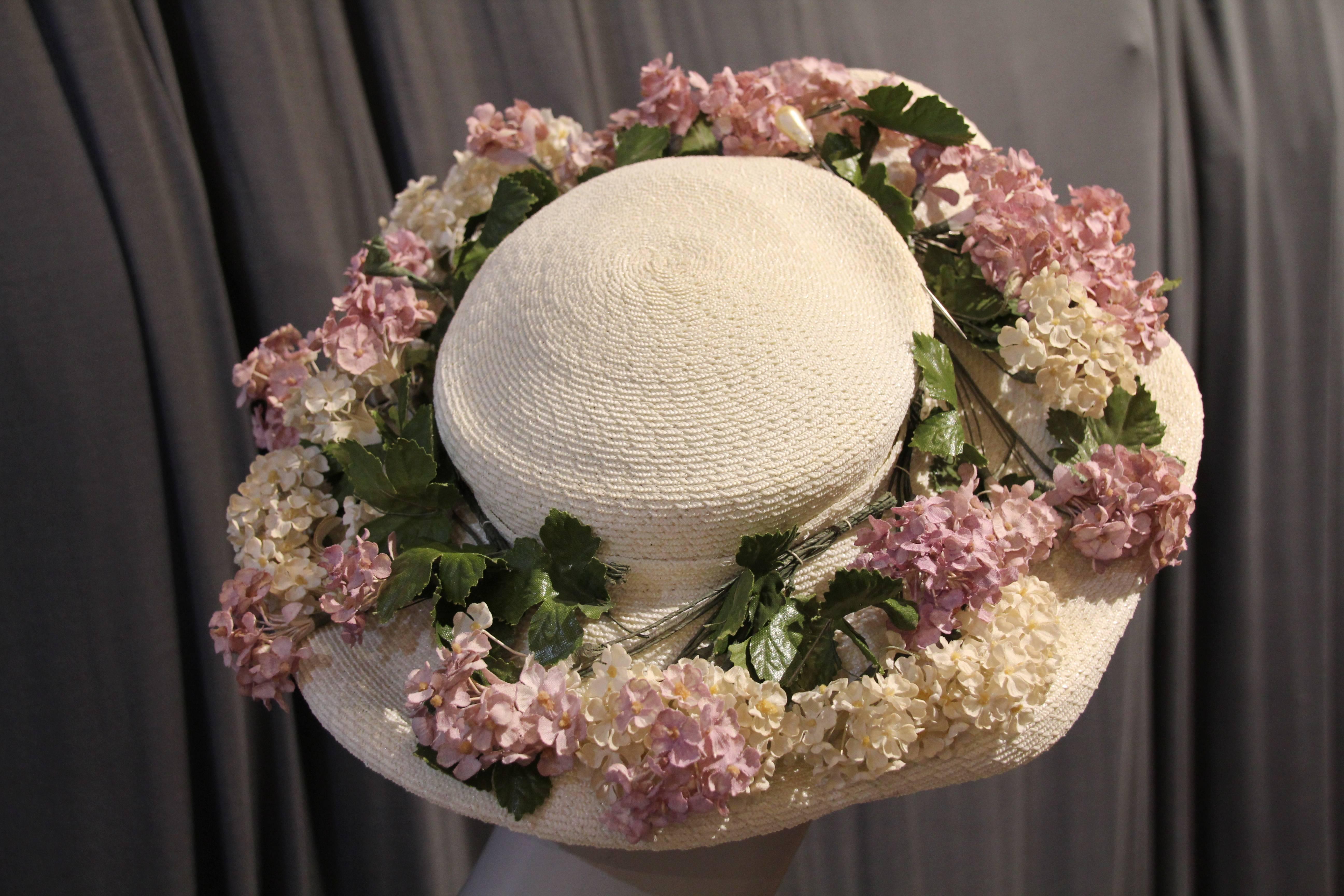 A charming 1950s Elsa Schiaparelli white straw hat with medium-sized brim and trimmed all around with lovely pale silk lilacs. One size fits all.  