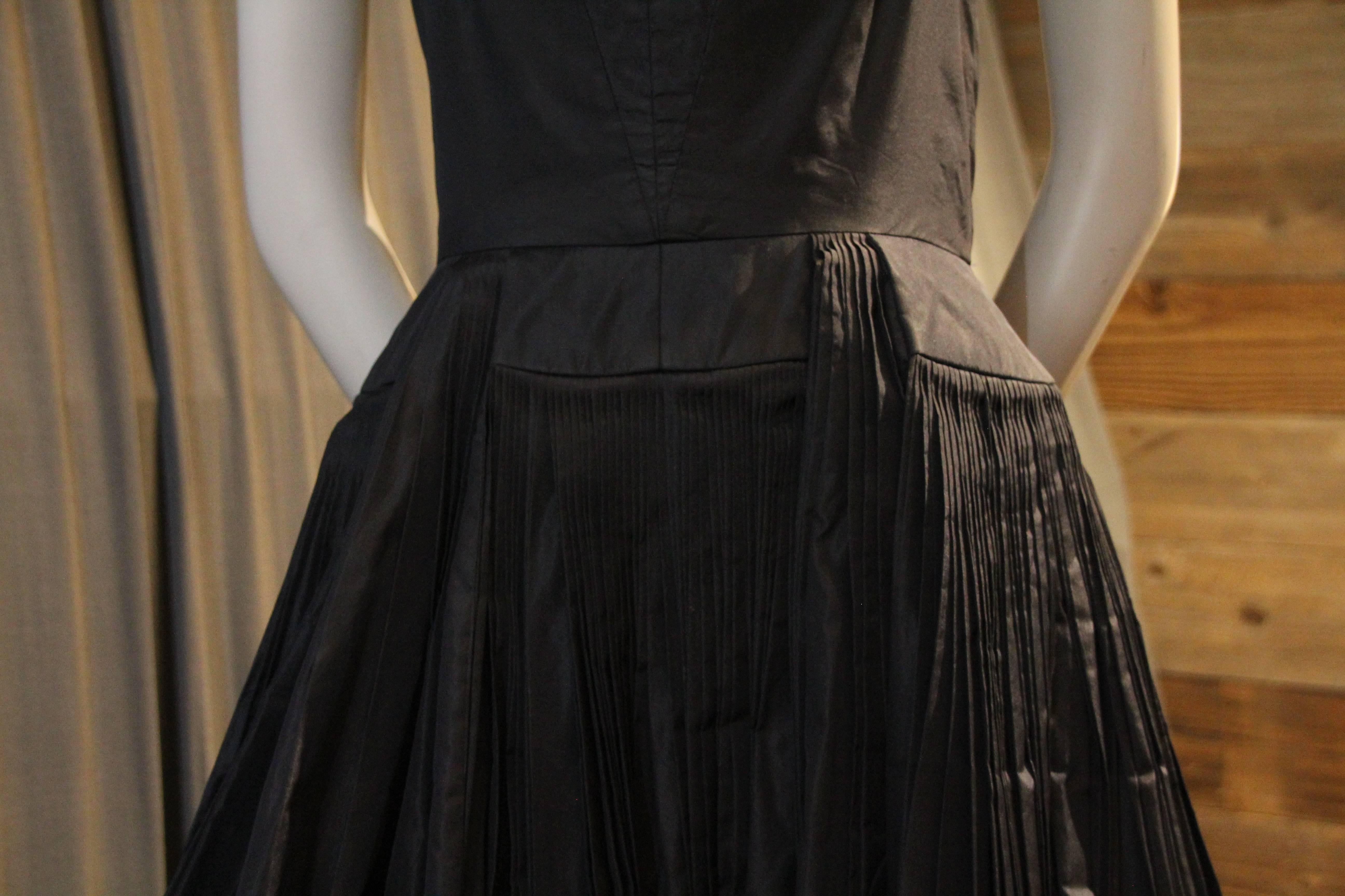 An exquisite 1950s James Galanos full-skirted black silk taffeta halter dress: Incredible and dense knife-pleats form the full circle skirt.  This is a couture quality dress executed in classic Galanos quality and style. 
