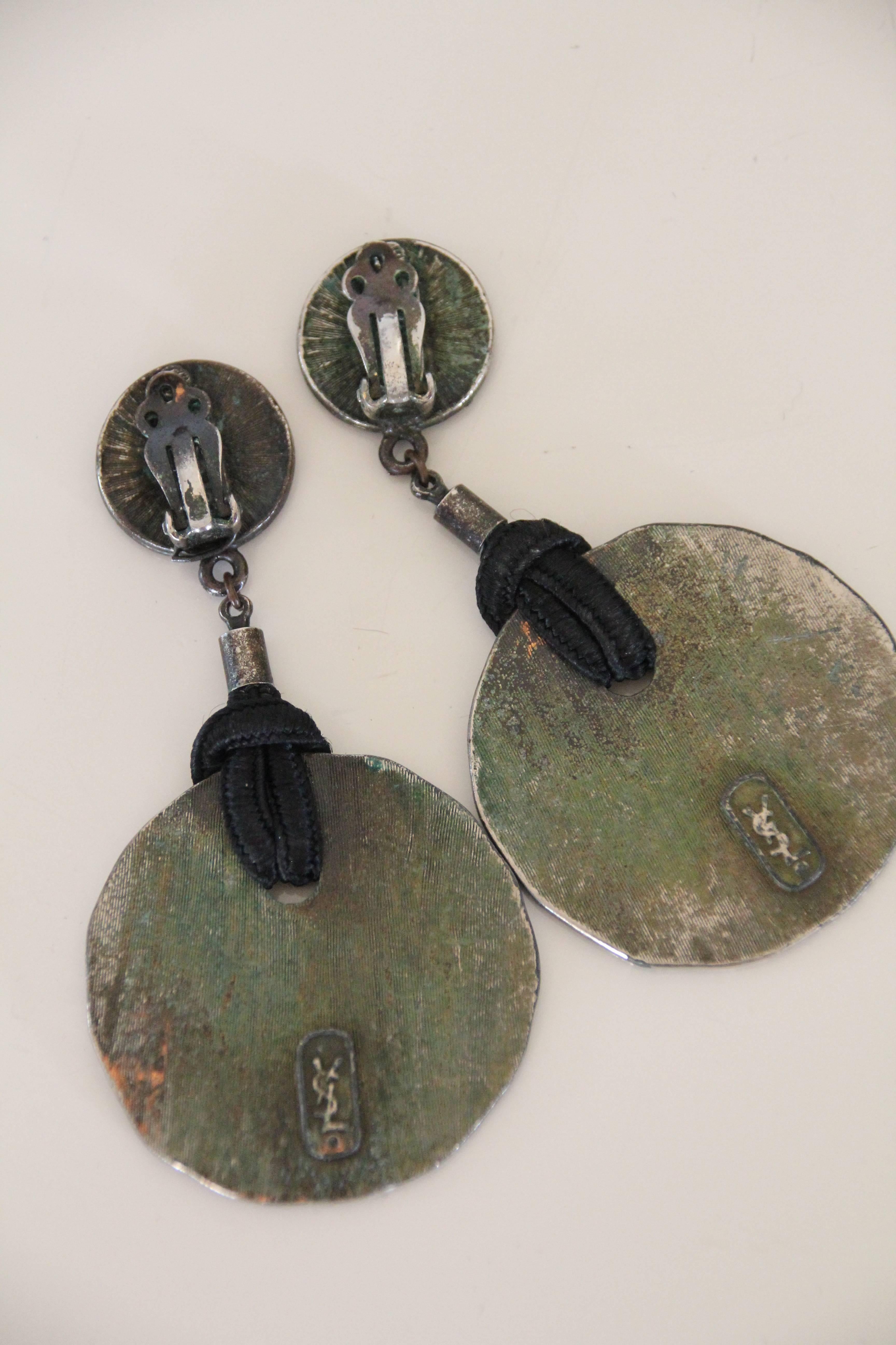A great casual jewelry set of earrings and a bolo tie: 1980s Yves Saint Laurent. Hammered bronze disc bolo tie with black cord and end caps. Matching hammered disc and leather dangle earrings with clip-on back. 