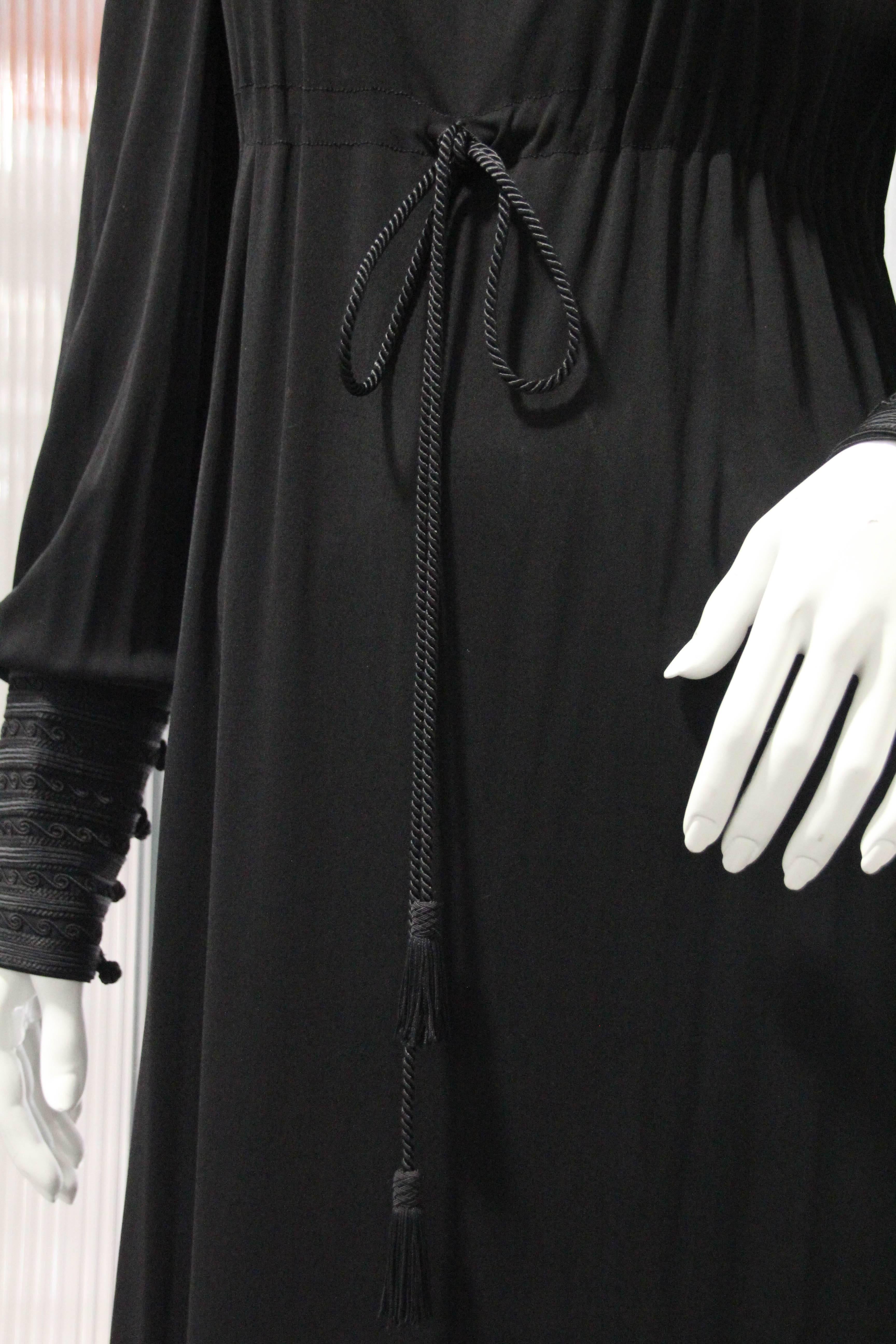 A beautiful 1970s Yves Saint Laurent black matte rayon jersey maxi dress with Moroccan-inspired style and braid trim at neckline. Draw string cord empire waist. Wide button and loop braid trimmed cuffs. Supremely comfortable, this piece has no
